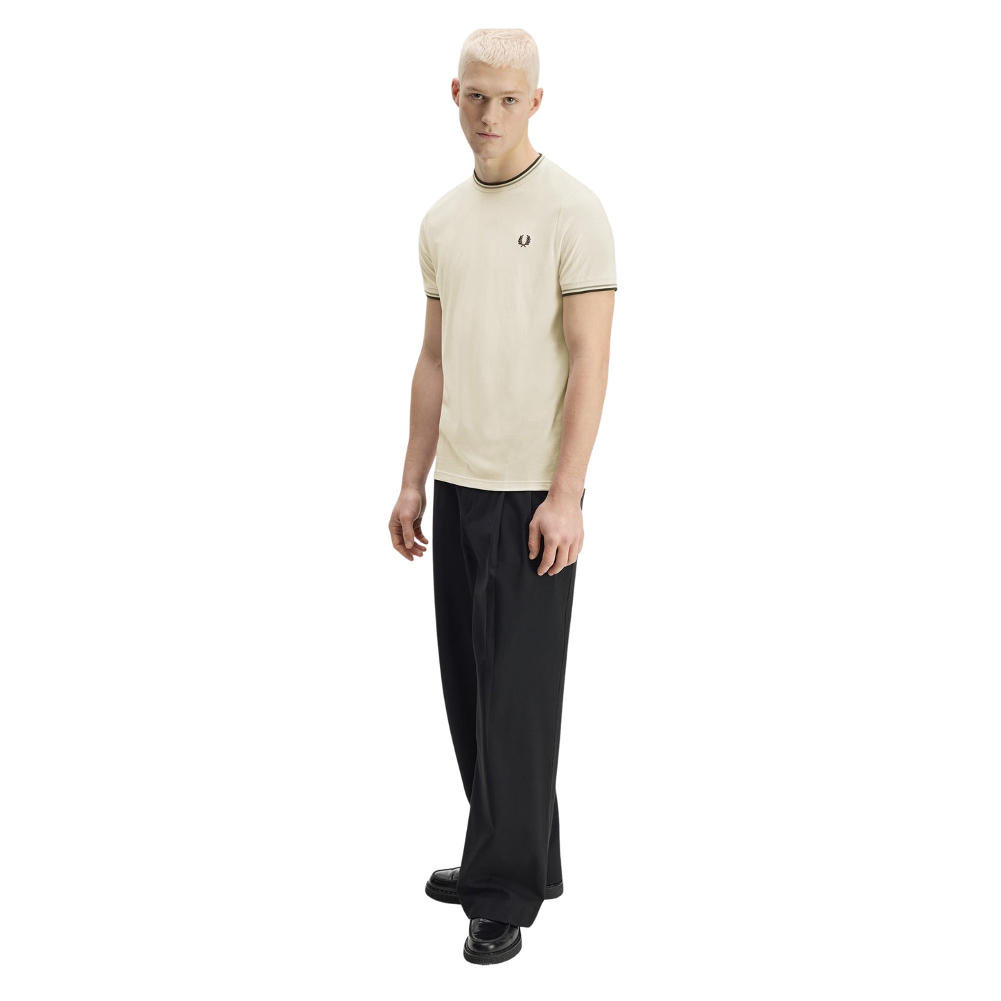 T-shirt Fred Perry Twin Tipped T-Shirt em Ecru — vista de três quartos com modelo, corpo inteiro, bordado Laurel Wreath em Dark Airforce no peito esquerdo e twin tipping no colarinho e punhos visíveis, combinado com calças pretas.
