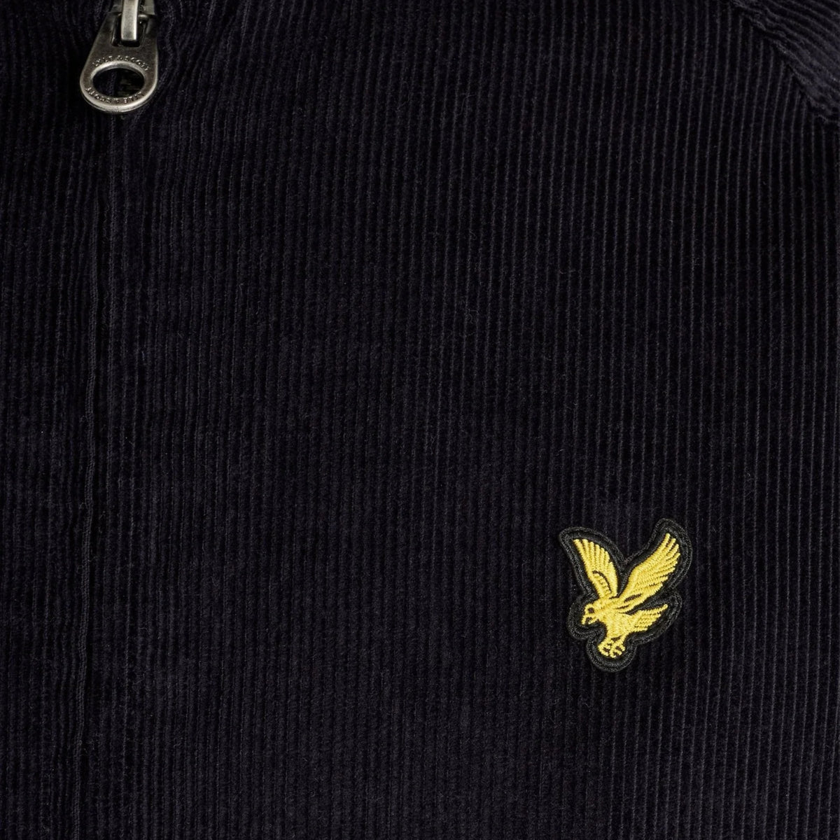 Pormenor da águia amarela bordada e da textura da bombazina azul-marinho do casaco Lyle & Scott Corduroy Harrington.