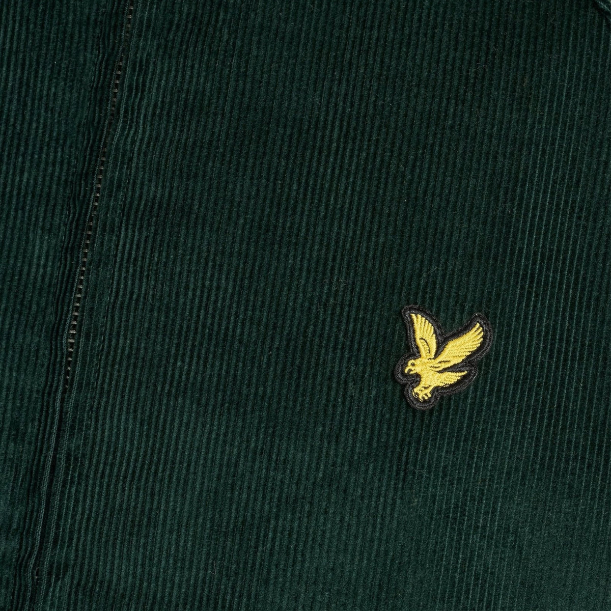 Pormenor da águia amarela bordada e da textura da bombazina verde-escura do casaco Lyle & Scott Corduroy Harrington.