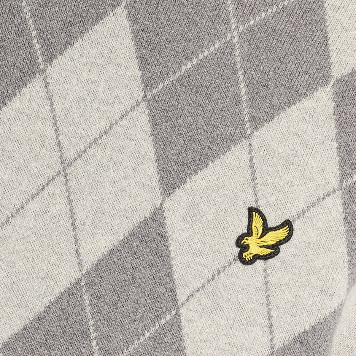 Pormenor da águia amarela bordada sobre o padrão de losangos da camisola Lyle & Scott Cotton Merino Argyle cinzenta.