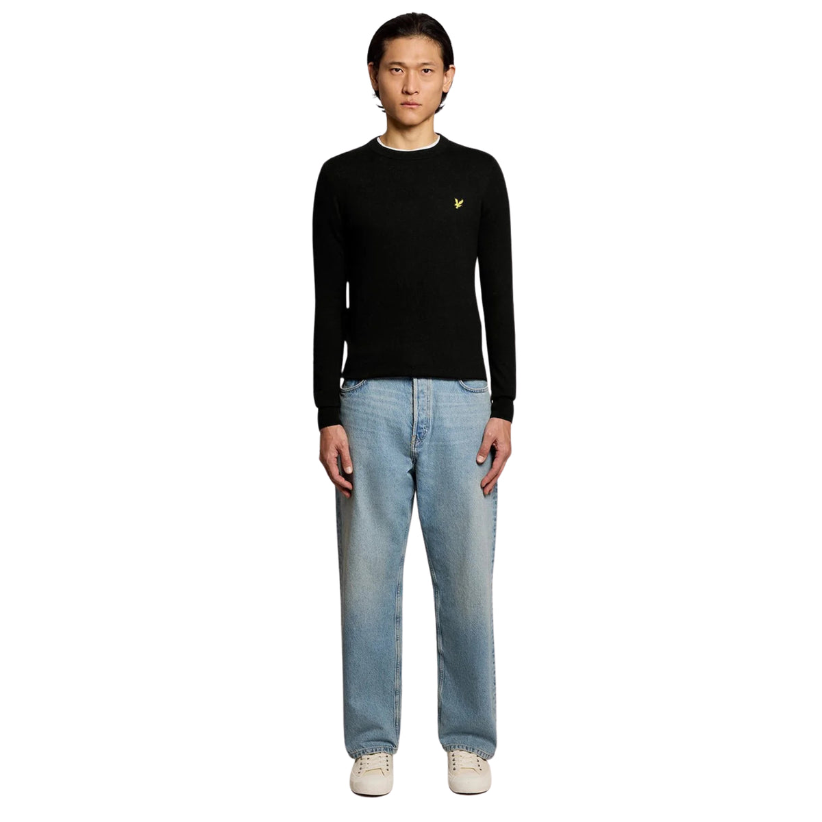 Modelo de corpo inteiro com camisola Lyle & Scott Cotton Merino Jet Black, calças de ganga claras e sapatilhas cru.
