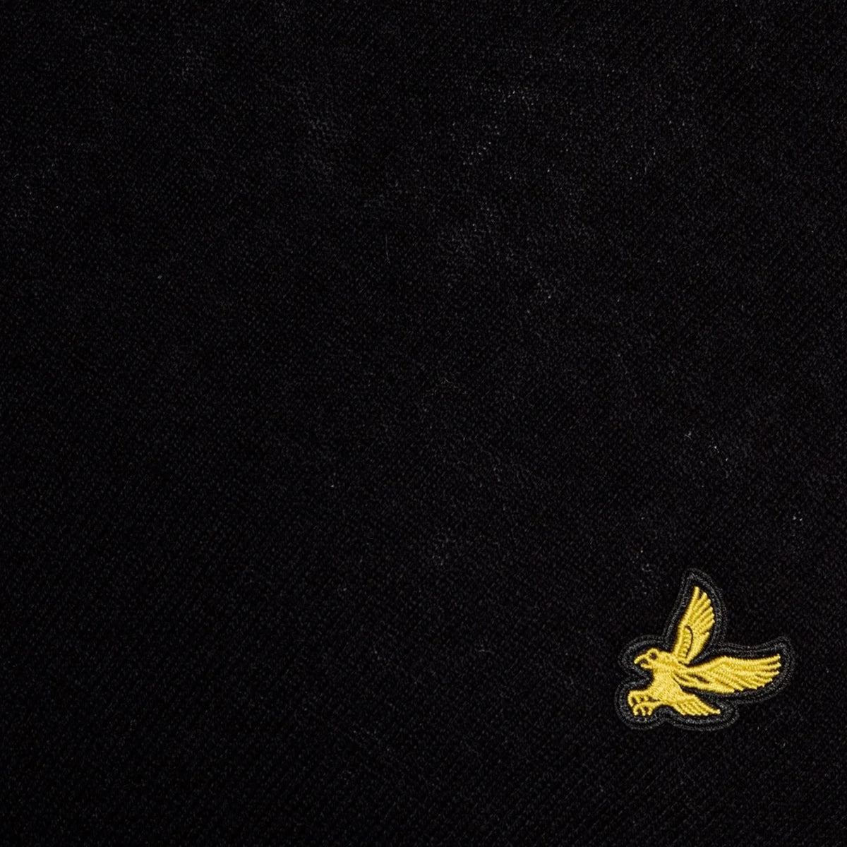 Pormenor da águia amarela bordada e da textura da malha preta da camisola Lyle & Scott Cotton Merino Jet Black.