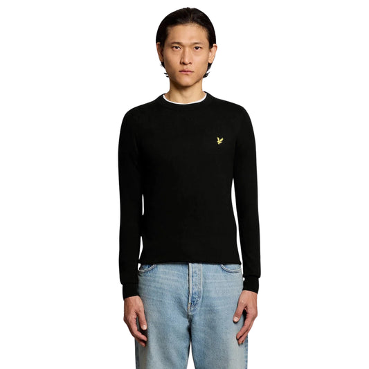 Camisola Lyle & Scott Cotton Merino em Jet Black vestida por modelo de frente, com gola redonda e águia amarela no peito.