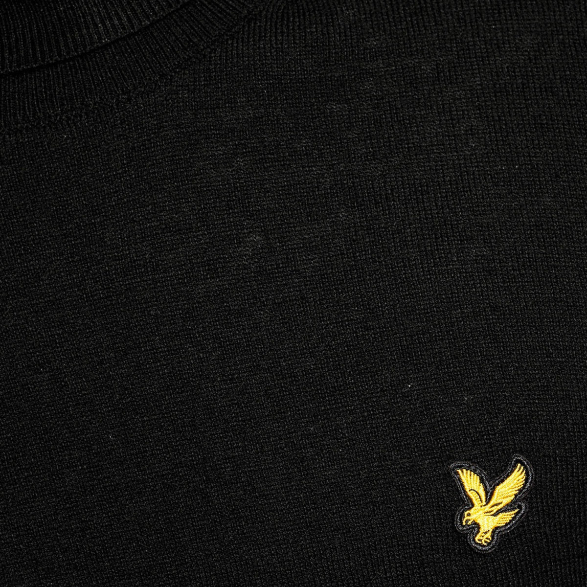Pormenor da textura da malha preta e da águia amarela bordada da camisola Lyle & Scott Cotton Merino Jet Black.