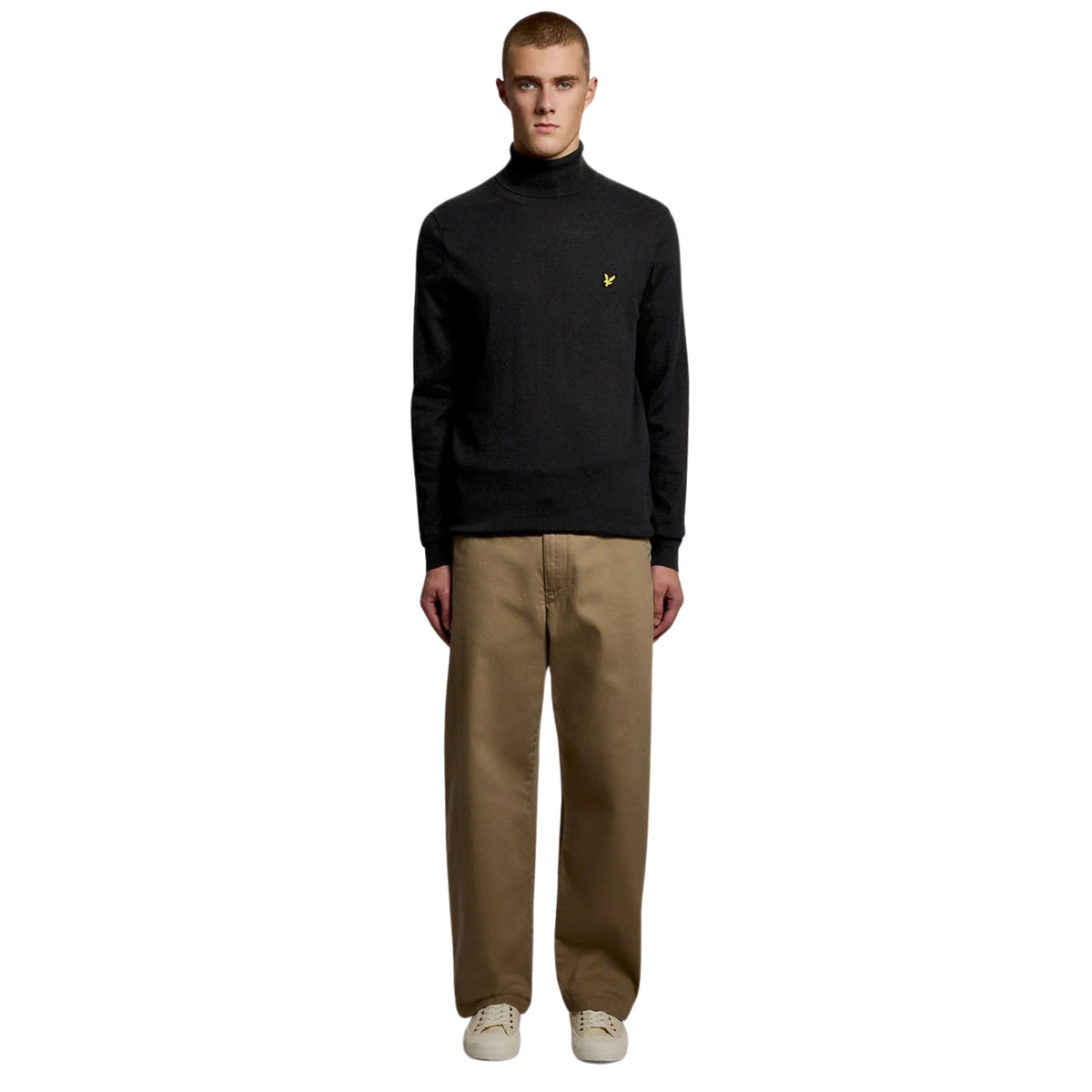 Modelo de corpo inteiro com camisola Lyle & Scott Cotton Merino Jet Black, calças bege e sapatilhas claras.