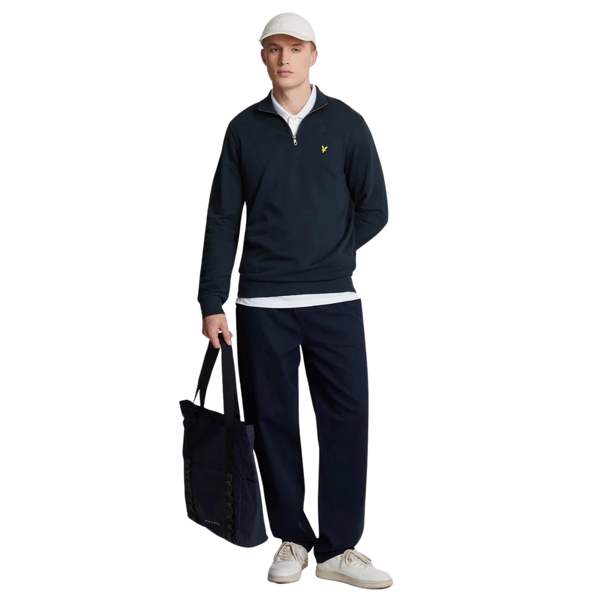 Modelo de corpo inteiro com sweat Lyle & Scott Loopback Dark Navy, calças escuras, boné claro e saco preto.