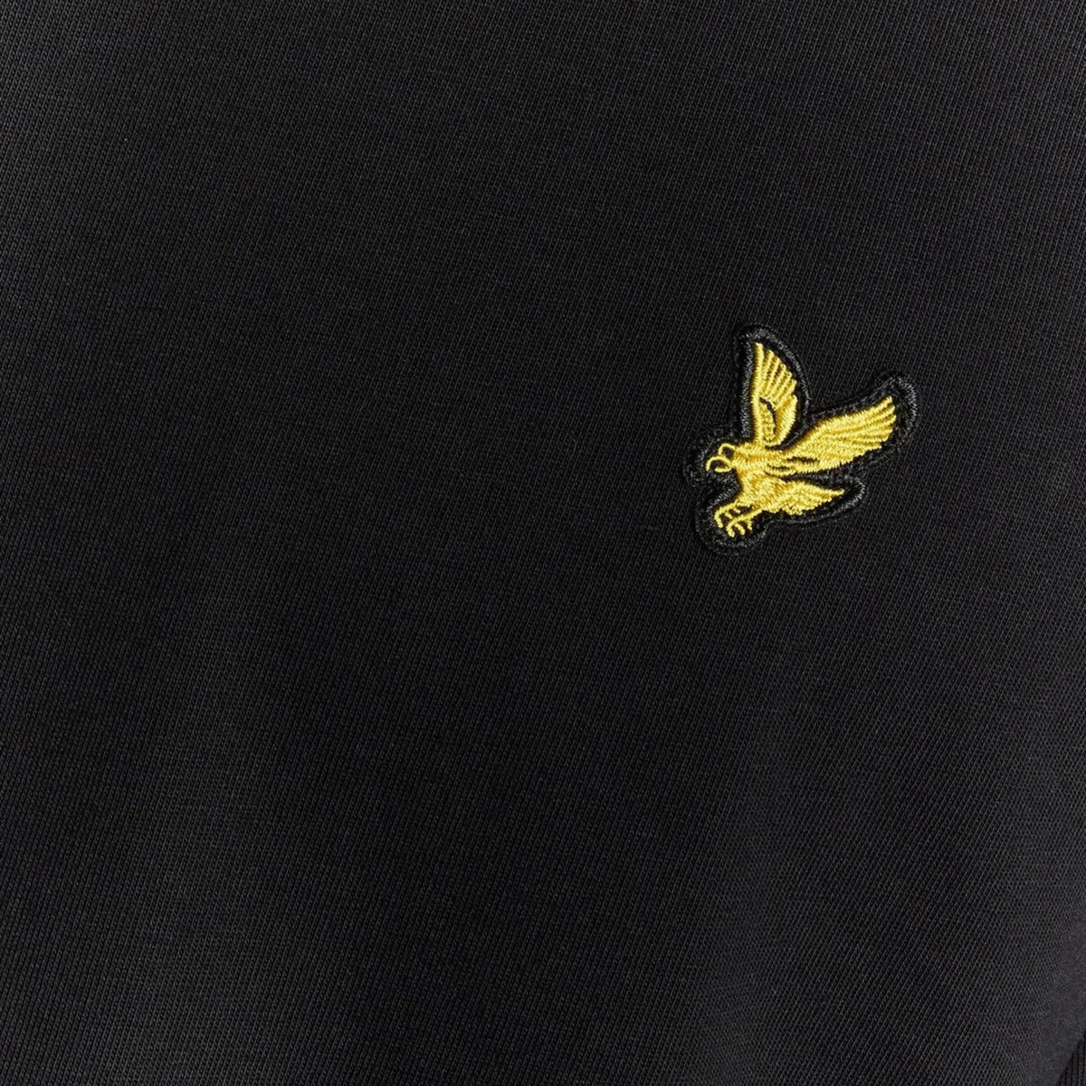 Pormenor da águia dourada bordada e da textura do tecido preto da t-shirt Lyle & Scott Plain.