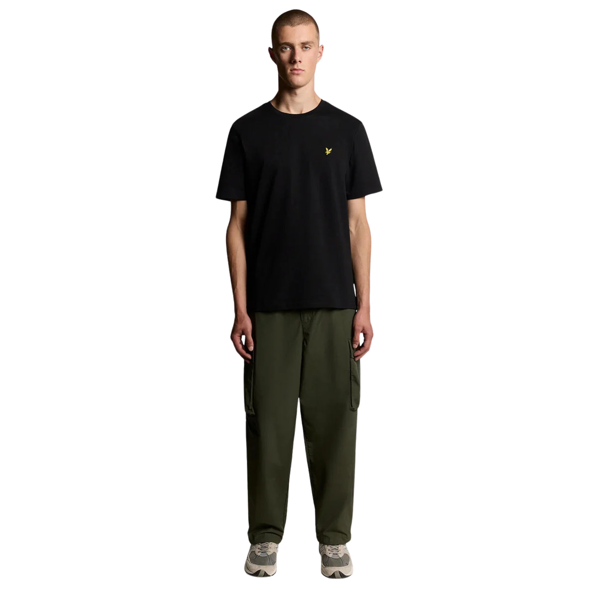 Modelo de corpo inteiro com t-shirt Lyle & Scott Plain Jet Black, calças cargo verde-azeitona e sapatilhas cinzentas.