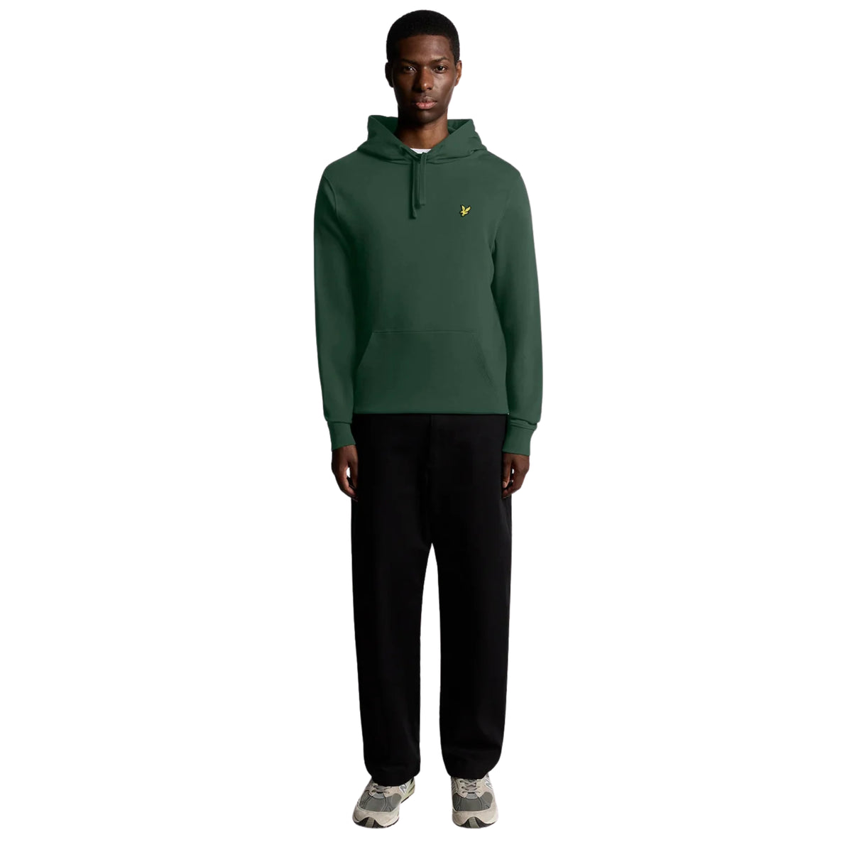 Modelo de corpo inteiro com hoodie Lyle & Scott Pullover Dark Green, calças pretas largas e sapatilhas cinzentas.