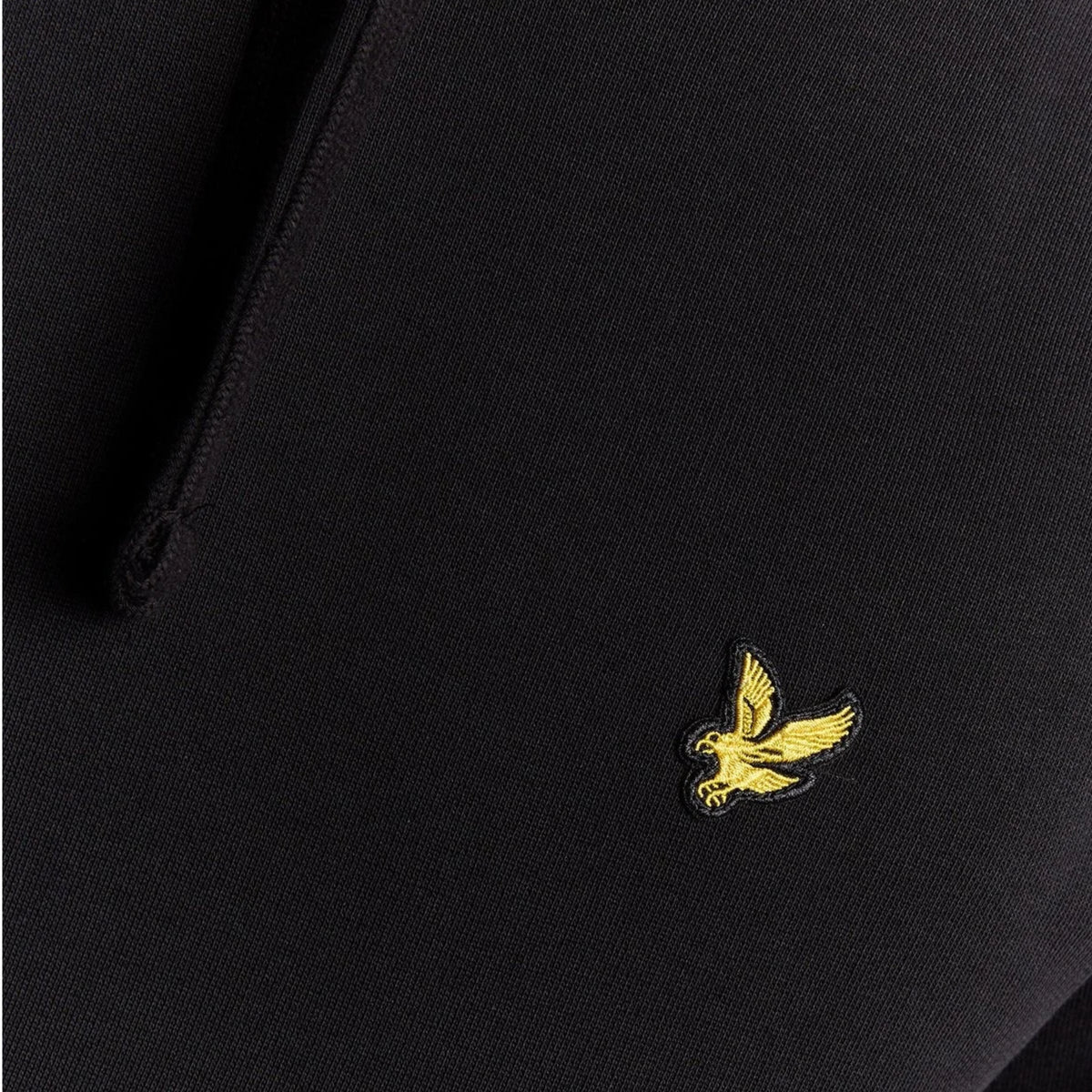 Pormenor da águia amarela bordada e da textura do tecido preto do hoodie Lyle & Scott Pullover.