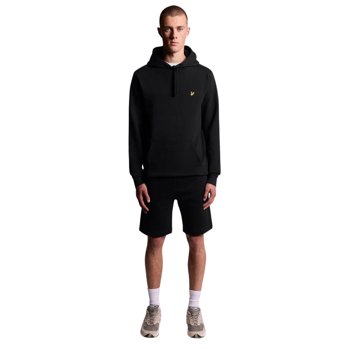 Modelo de corpo inteiro com hoodie Lyle & Scott Pullover Jet Black, calções pretos, meias brancas e sapatilhas cinzentas.
