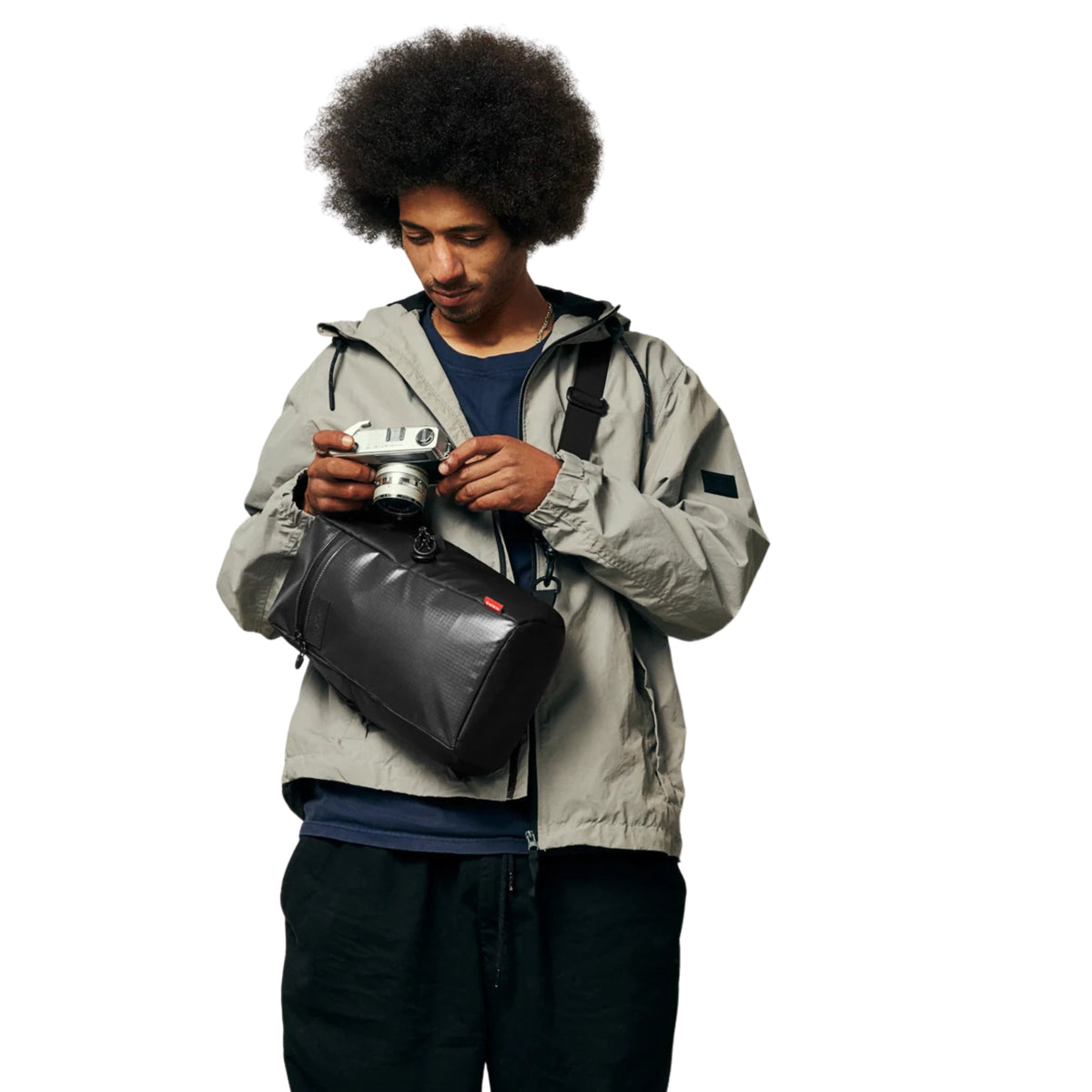 Modelo com a bolsa Nixon Syndicate Sling Bag Asphalt a tiracolo à frente do corpo, enquanto segura uma máquina fotográfica.