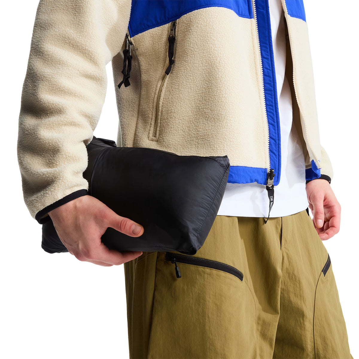 Casaco The North Face 1996 Retro Nuptse preto acondicionado no próprio bolso, formando um volume compacto transportado na mão pelo modelo.