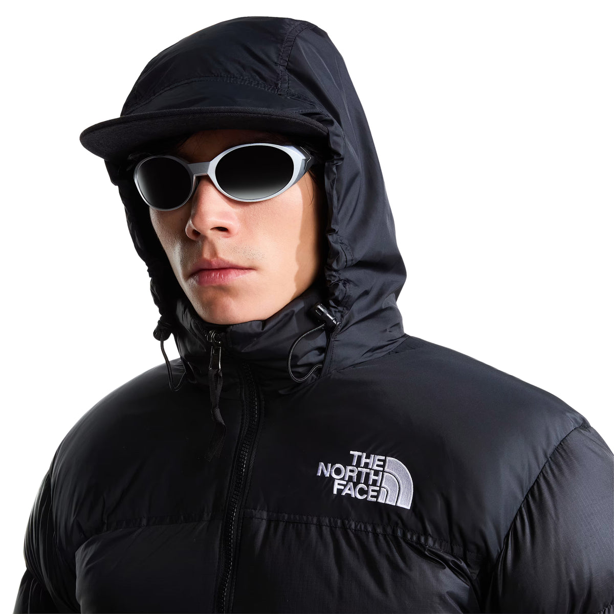 Pormenor do casaco The North Face 1996 Retro Nuptse preto em modelo com capuz colocado, mostrando os ajustes laterais e o logótipo branco no peito.