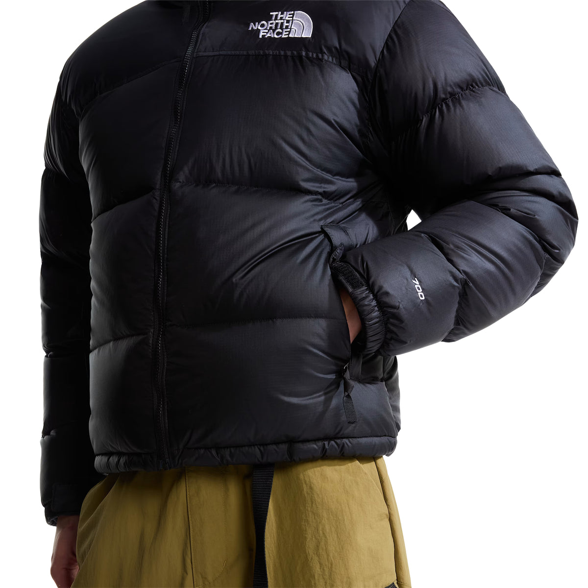 Pormenor frontal do casaco The North Face 1996 Retro Nuptse preto, com a mão no bolso lateral, painéis acolchoados e bordado 700 na manga.