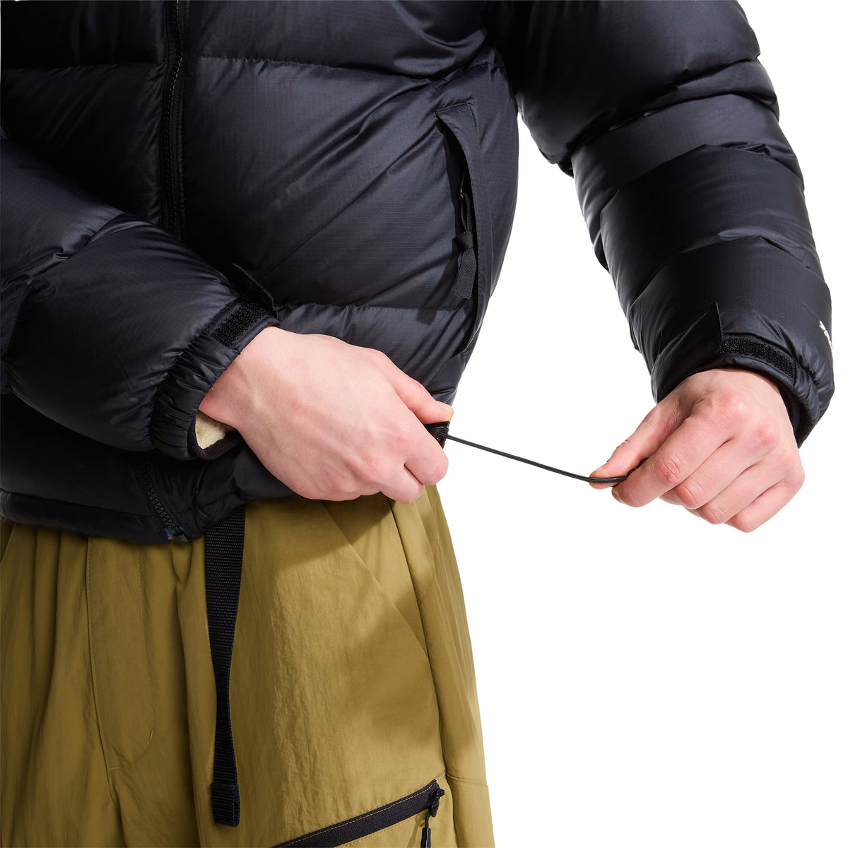 Pormenor do casaco The North Face 1996 Retro Nuptse preto, com o modelo a puxar o cordão de ajuste da bainha.