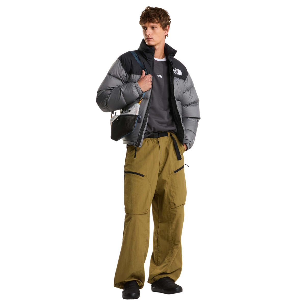 Modelo de corpo inteiro com o casaco The North Face 1996 Retro Nuptse Smoked Pearl/TNF Black aberto e mala ao ombro.