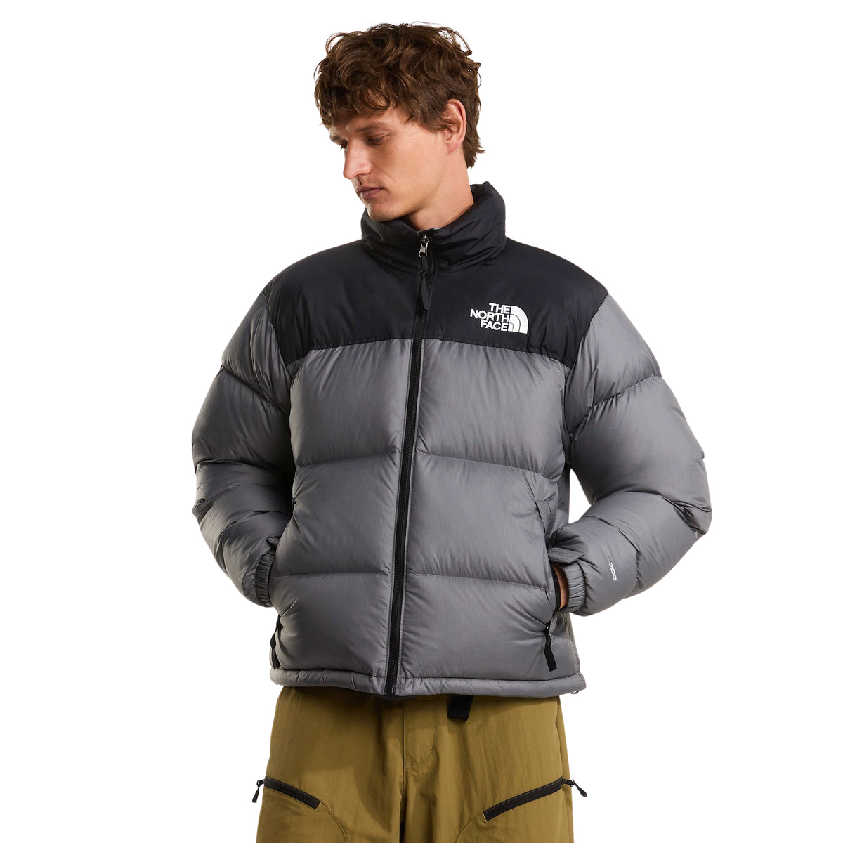 Casaco The North Face 1996 Retro Nuptse Smoked Pearl/TNF Black vestido de frente, com fecho fechado e mãos nos bolsos.