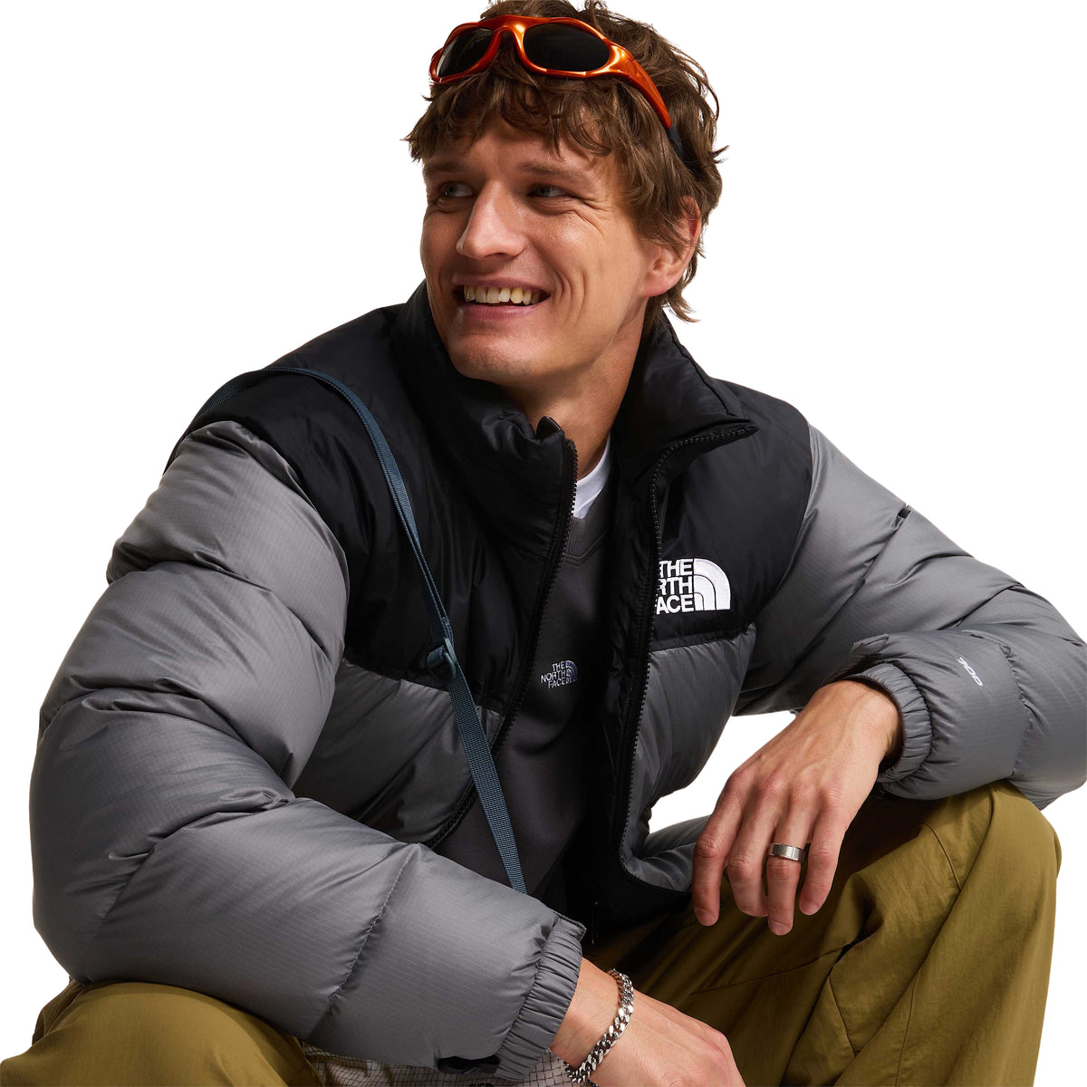 Casaco The North Face 1996 Retro Nuptse cinzento e preto vestido por modelo agachado, com fecho aberto.