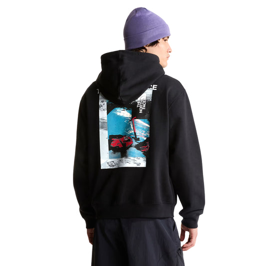 Hoodie The North Face Apex '75 Collage Relaxed em TNF Black — modelo masculino de costas a 3/4, gorro TNF lilás/roxo, calças cargo azul-marinho escuro, gráfico collage Apex '75 em caixa com esquiador em neve azul-glaciar e logo TNF em branco nas costas visíveis, fundo branco.