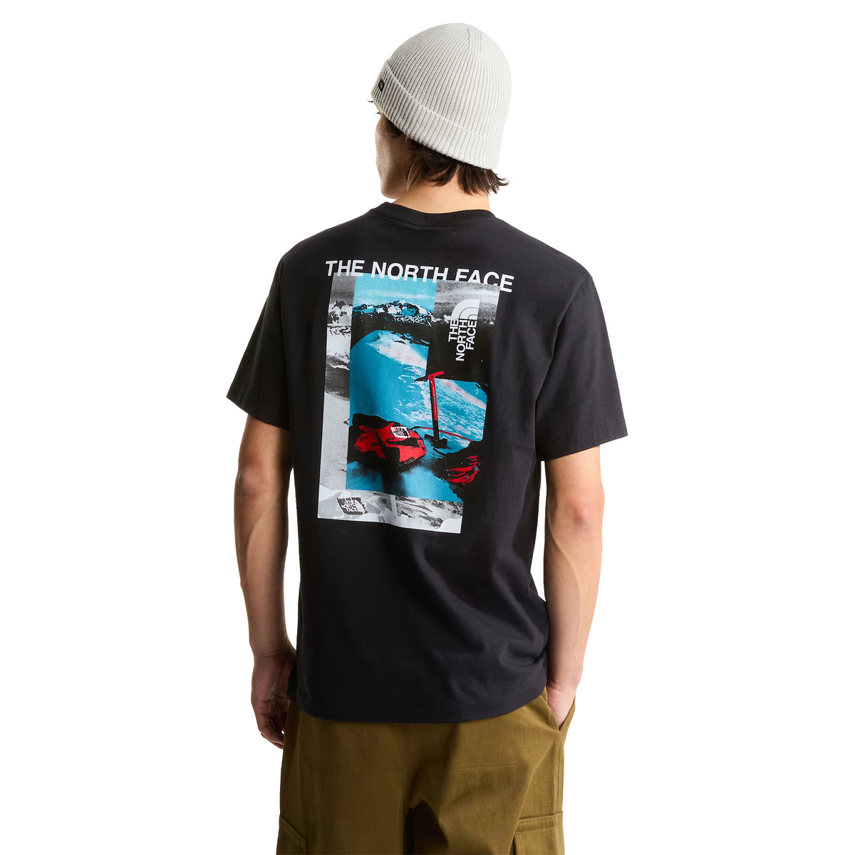 T-shirt de manga curta The North Face Apex '75 Collage em preto — modelo masculino de costas, pormenor do gráfico collage: "THE NORTH FACE" em branco, collage com montanha nevada em azul, luvas de ski vermelhas TNF, logótipo TNF vertical, gorro cinzento, fundo branco.