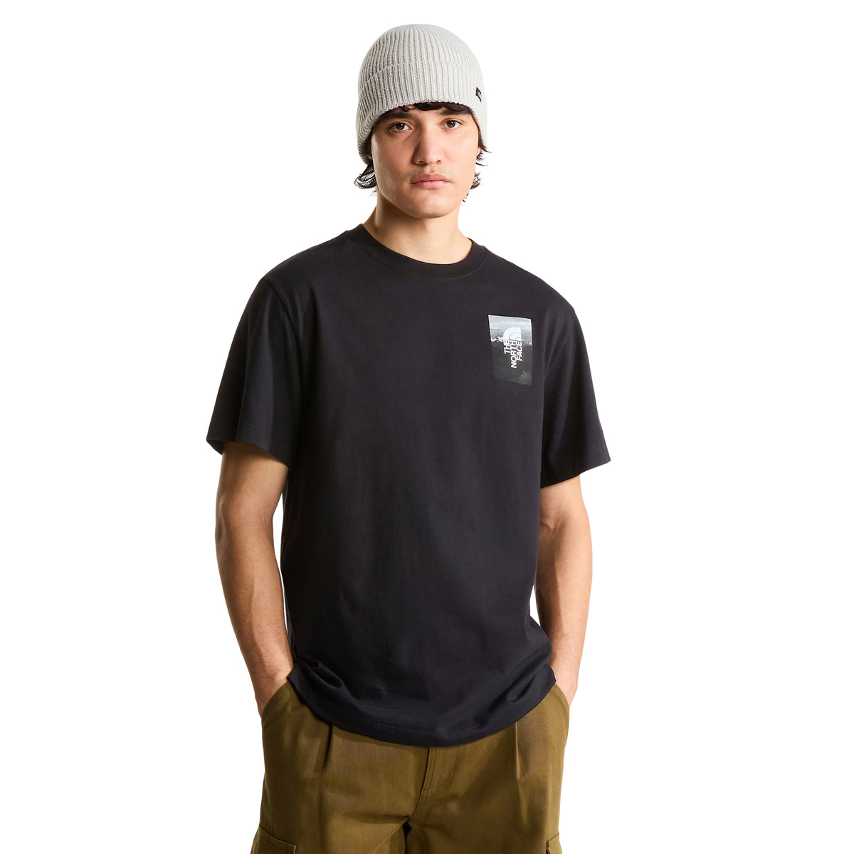 T-shirt de manga curta The North Face Apex '75 Collage em preto — modelo masculino de frente, meio corpo, t-shirt preta com logótipo The North Face no peito esquerdo, gola redonda canelada, corte relaxed, calças cargo camel, gorro cinzento, fundo branco.
