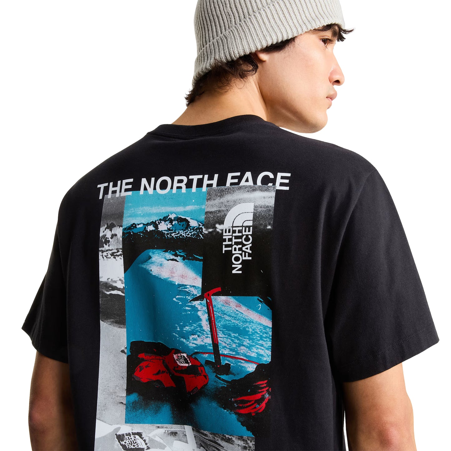 pormenor de costas com modelo (meio corpo, costas/ombro de lado direito), gráfico collage visível: "THE NORTH FACE" em branco, paisagem nevada azul, luvas e piolet vermelhos TNF, logótipo TNF quadrado.