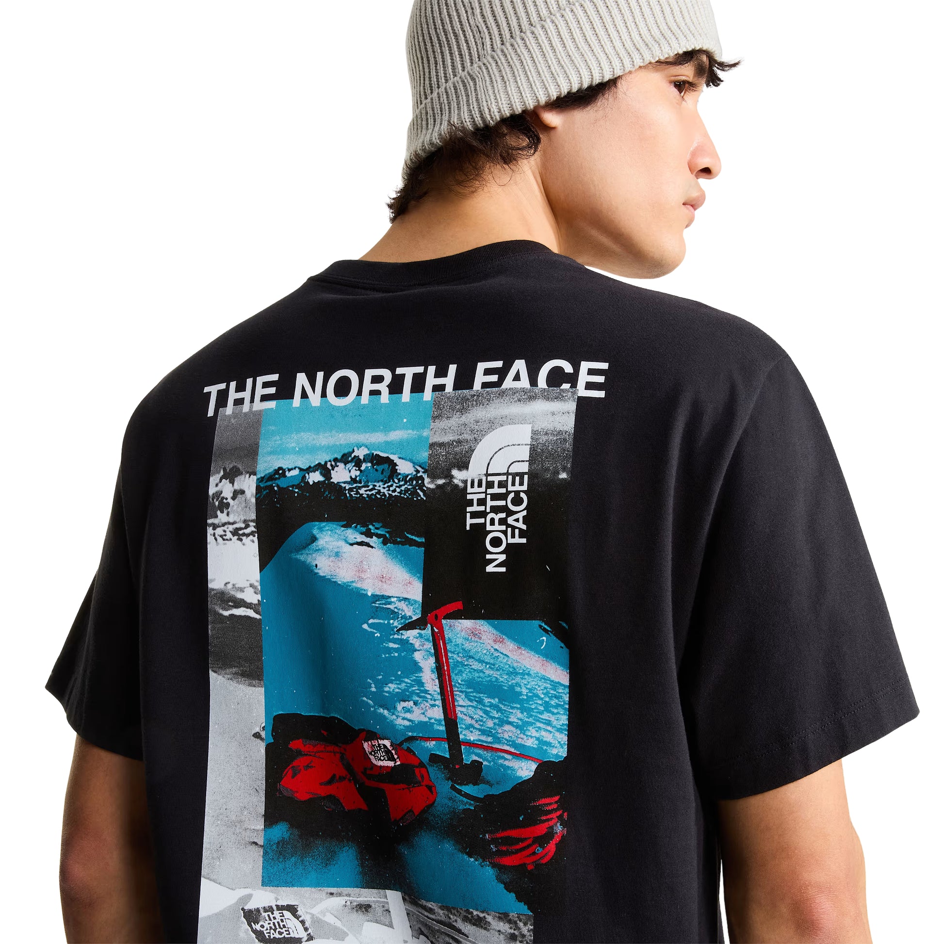 pormenor de costas com modelo (meio corpo, costas/ombro de lado direito), gráfico collage visível: "THE NORTH FACE" em branco, paisagem nevada azul, luvas e piolet vermelhos TNF, logótipo TNF quadrado.