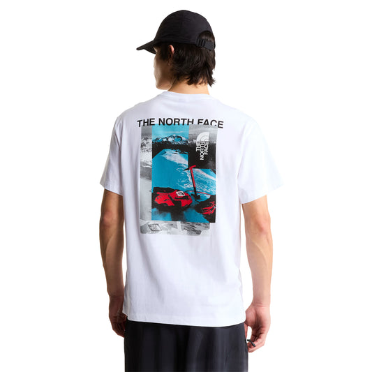 T-shirt de manga curta The North Face Apex '75 Collage em branco — modelo masculino de costas, corpo inteiro, gráfico collage com "THE NORTH FACE" em preto, paisagem de montanha nevada em azul/cinzento, luvas e equipamento de ski vermelho TNF, corte relaxed, boné preto, calças pretas, fundo branco.