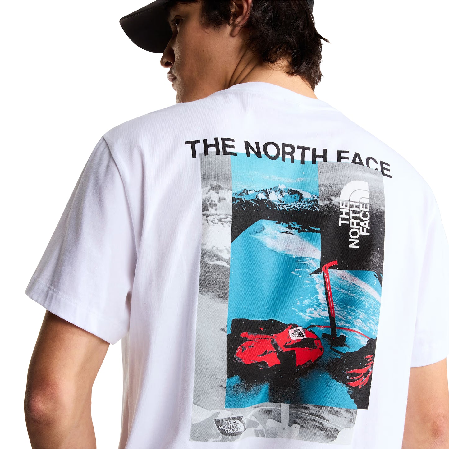 T-shirt de manga curta The North Face Apex '75 Collage em branco — modelo masculino de costas, meio corpo, gráfico collage Apex '75 com "THE NORTH FACE" em preto, paisagem nevada em azul/cinzento, luvas de ski vermelhas TNF e logótipo TNF vertical, mochila crossbody cinzenta em ripstop a tiracolo, boné preto, fundo branco.