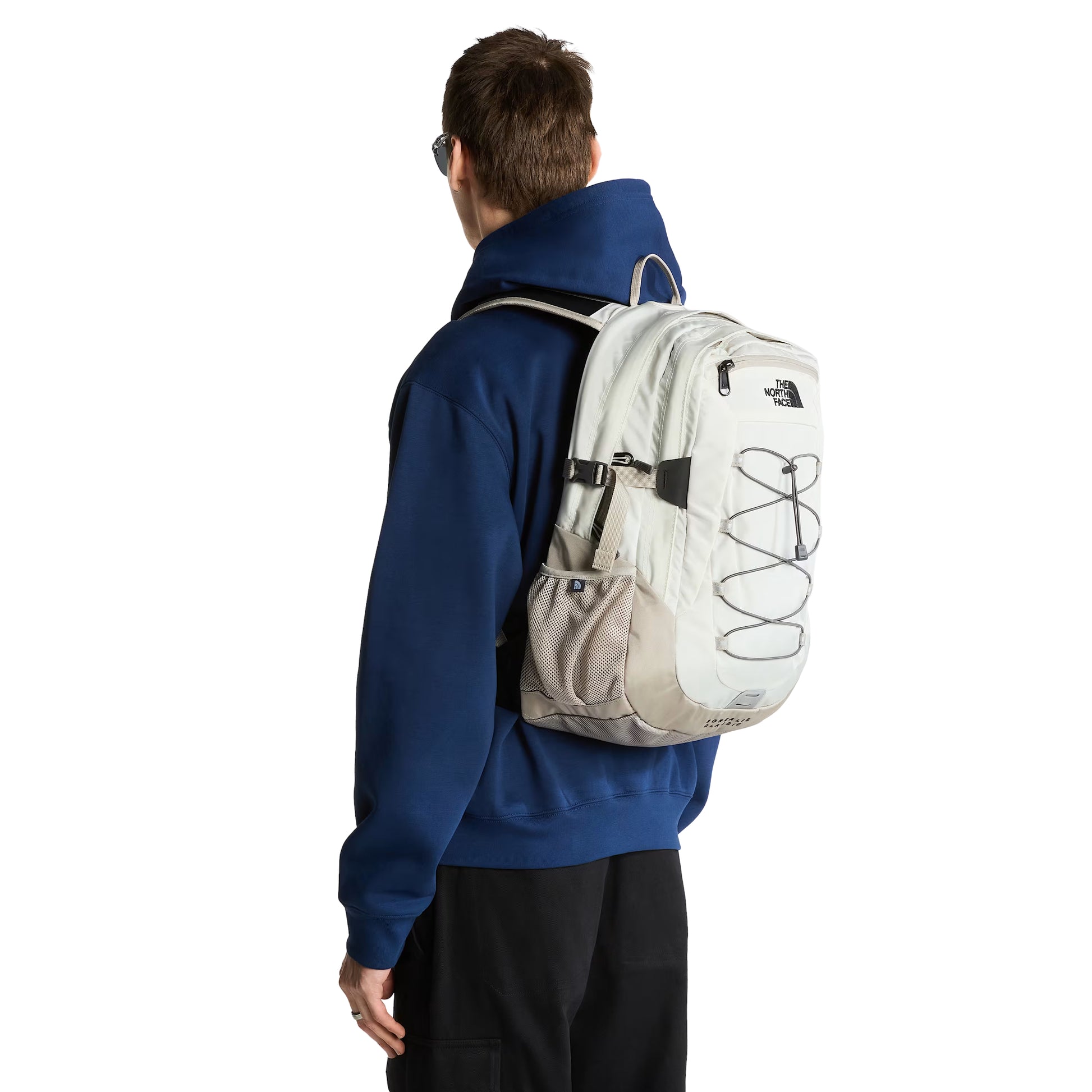 Mochila The North Face Borealis Classic em Cumulus Cloud / Stone Slab — modelo masculino de costas, hoodie azul marinho, calças pretas, vista traseira da mochila com logo TNF bordado em preto, sistema de cordas elásticas Anthracite Grey, bolso lateral em malha Stone Slab e inscrição "Borealis Classic" na base visíveis.