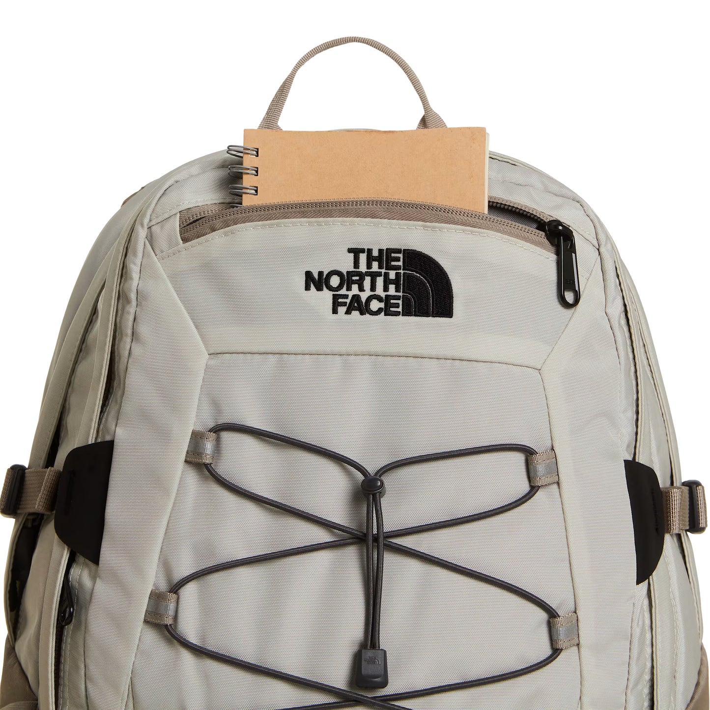 Mochila The North Face Borealis Classic em Cumulus Cloud / Stone Slab — detalhe do topo com bolso zip aberto e caderno kraft, logo The North Face bordado em preto e sistema de cordas elásticas Anthracite Grey visíveis, fundo branco.