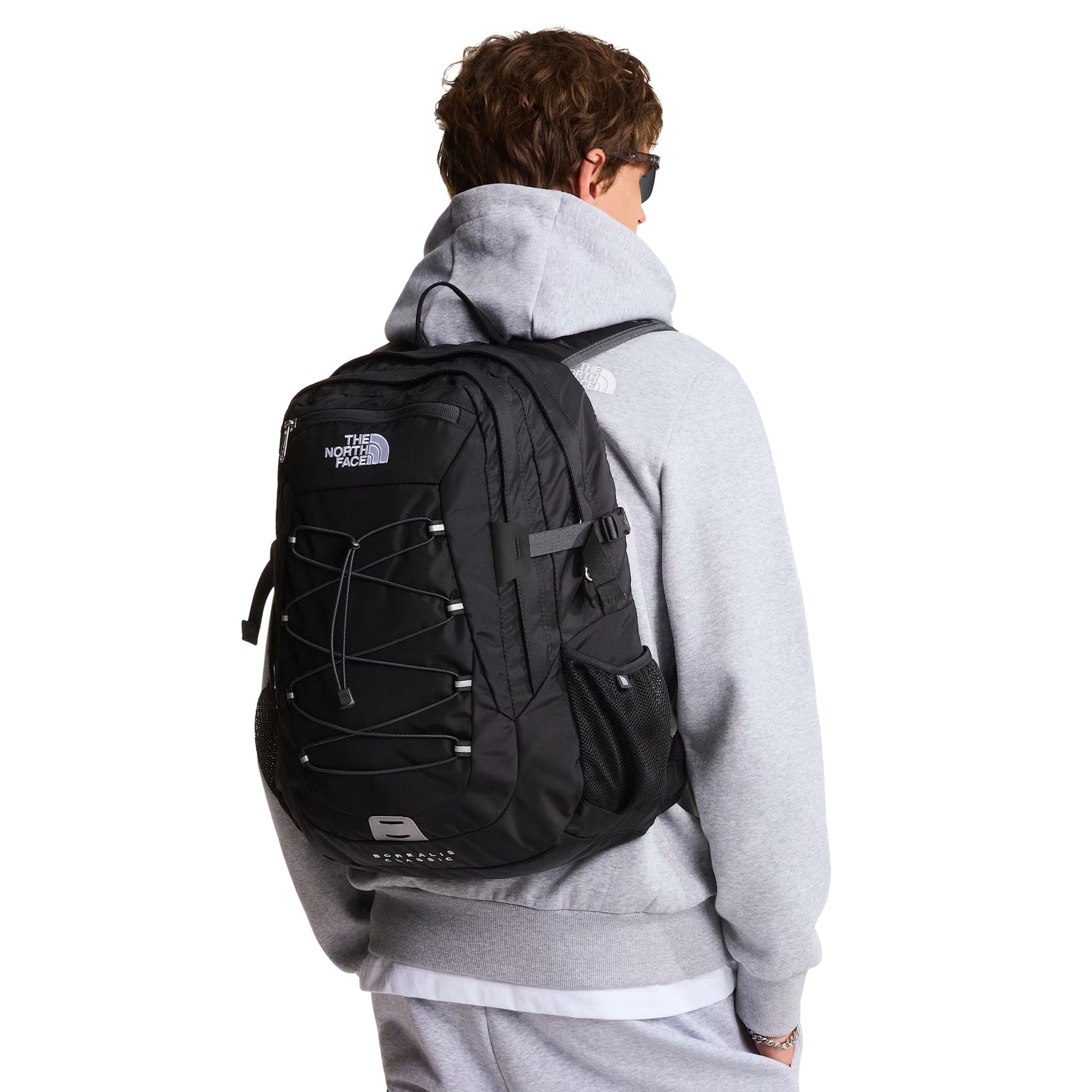 Mochila The North Face Borealis Classic em TNF Black / Asphalt Grey — vista frontal com modelo de costas, sweat cinzenta clara, mochila ajustada ao corpo com logo TNF bordado em branco, sistema de cordas elásticas e bolso lateral em malha visíveis.