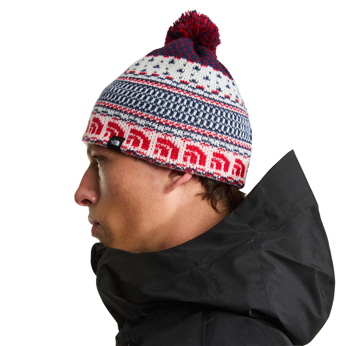 Vista lateral do gorro The North Face Cabin Ski Tuke White Dune Jacquard num modelo, mostrando o pompom e a etiqueta com logótipo.