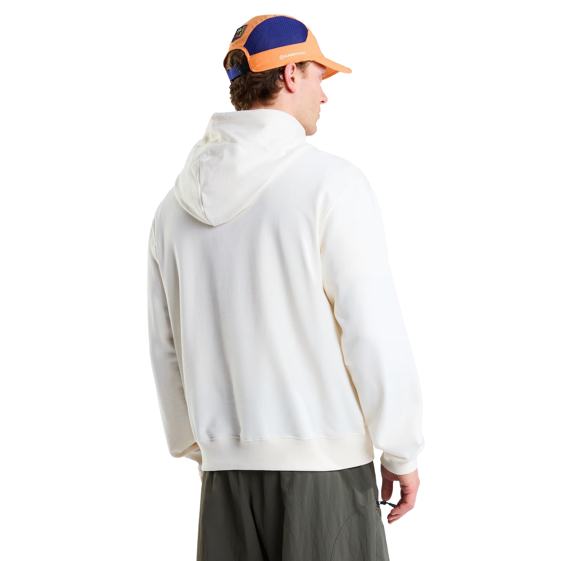 Hoodie unissexo The North Face Explorer Badges Relaxed em White Dune — modelo masculino de costas, boné técnico laranja TNF, óculos de sol wrap escuros, calças cargo verde-oliva, capuz levantado, logótipo "The North Face" half-dome estampado em serigrafia à base de água no ombro direito nas costas visível, corte relaxado com ombros descaídos, French Terry White Dune 360 g/m², fundo branco.