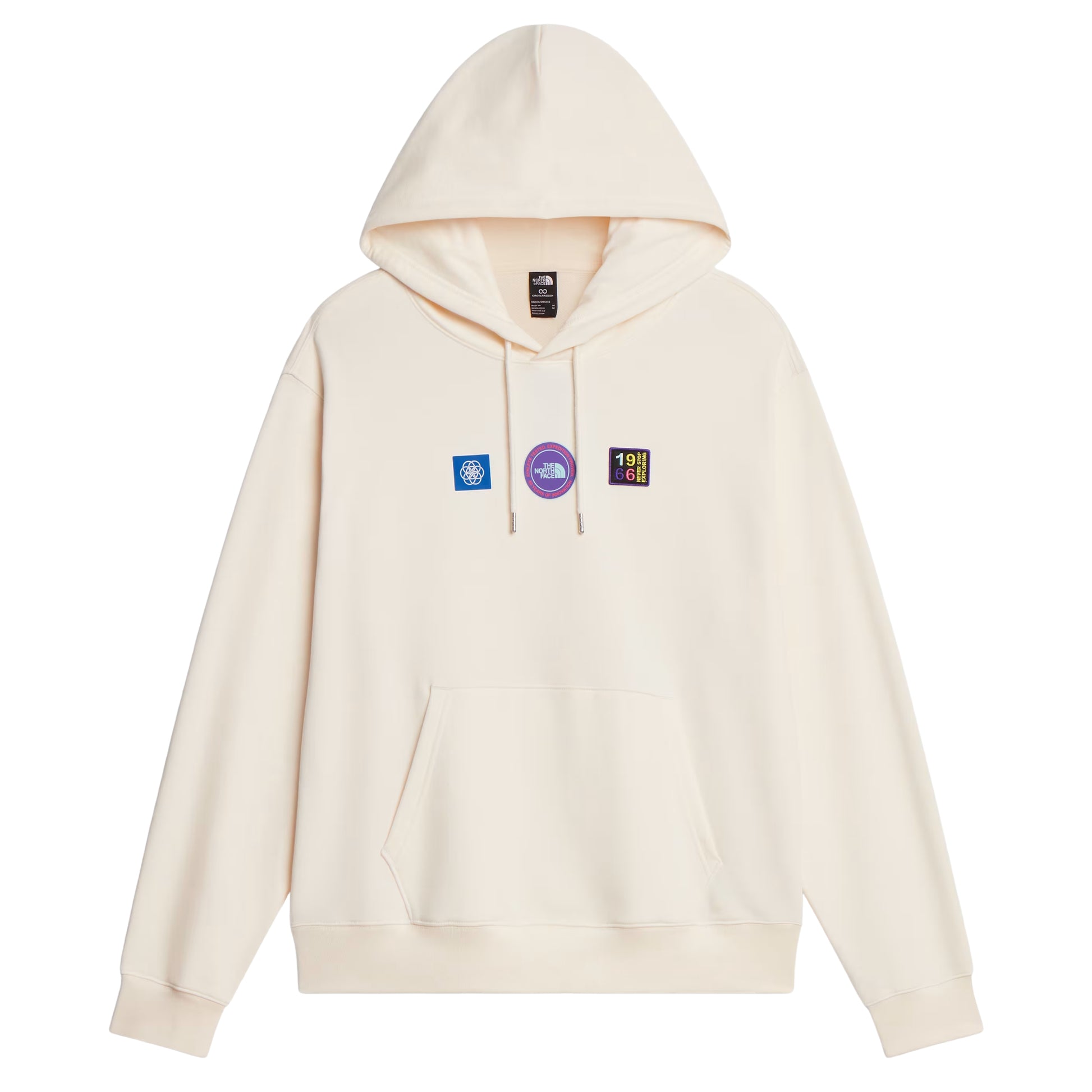 Hoodie unissexo The North Face Explorer Badges Relaxed em White Dune — vista frontal, produto sem modelo, etiqueta TNF na gola interior visível, três emblemas Explorer estampados em serigrafia à base de água no peito (azul quadrado com globo, circular roxo "The North Face", retangular escuro "1966 Never Stop Exploring" multicolor), capuz com cordão branco, bolso canguru e bainha canelada visíveis, French Terry White Dune 360 g/m², fundo branco.