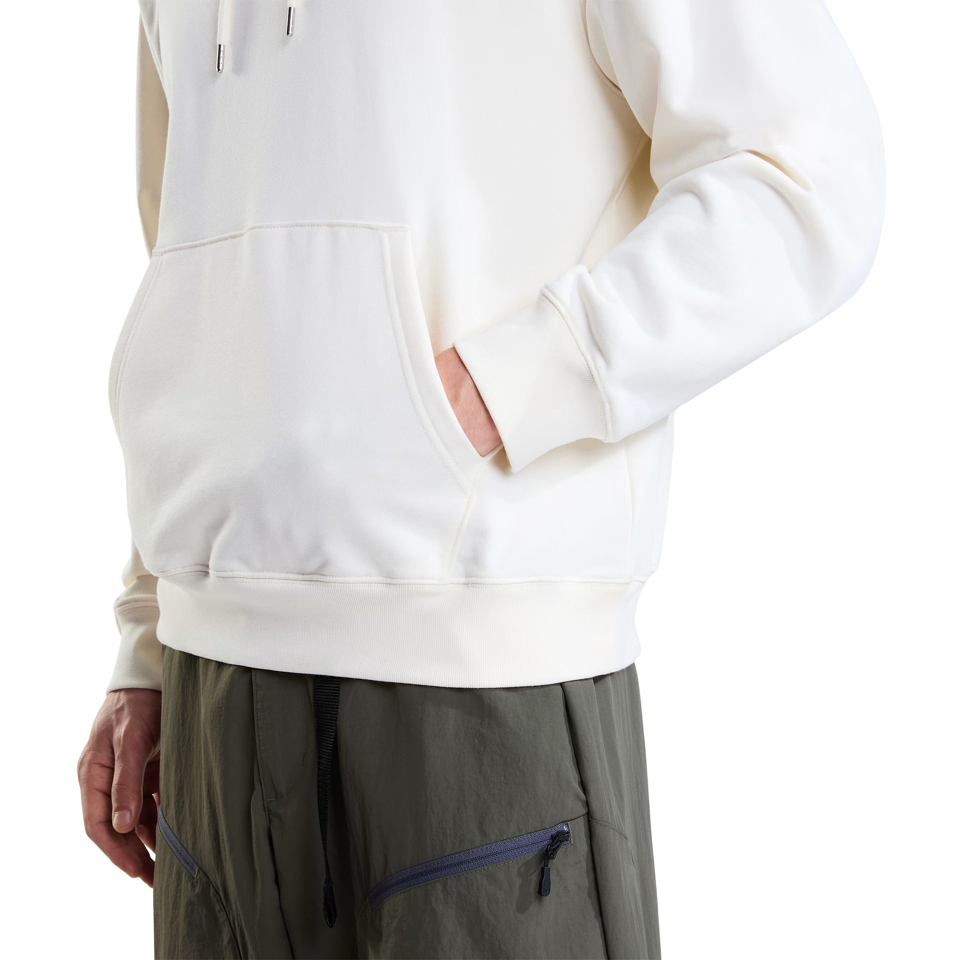 Hoodie unissexo The North Face Explorer Badges Relaxed em White Dune — modelo masculino, detalhe da parte inferior, meio corpo, calças cargo verde-oliva TNF, mão no bolso canguru, bainha canelada e punho canelado visíveis, French Terry White Dune 360 g/m², fundo branco.