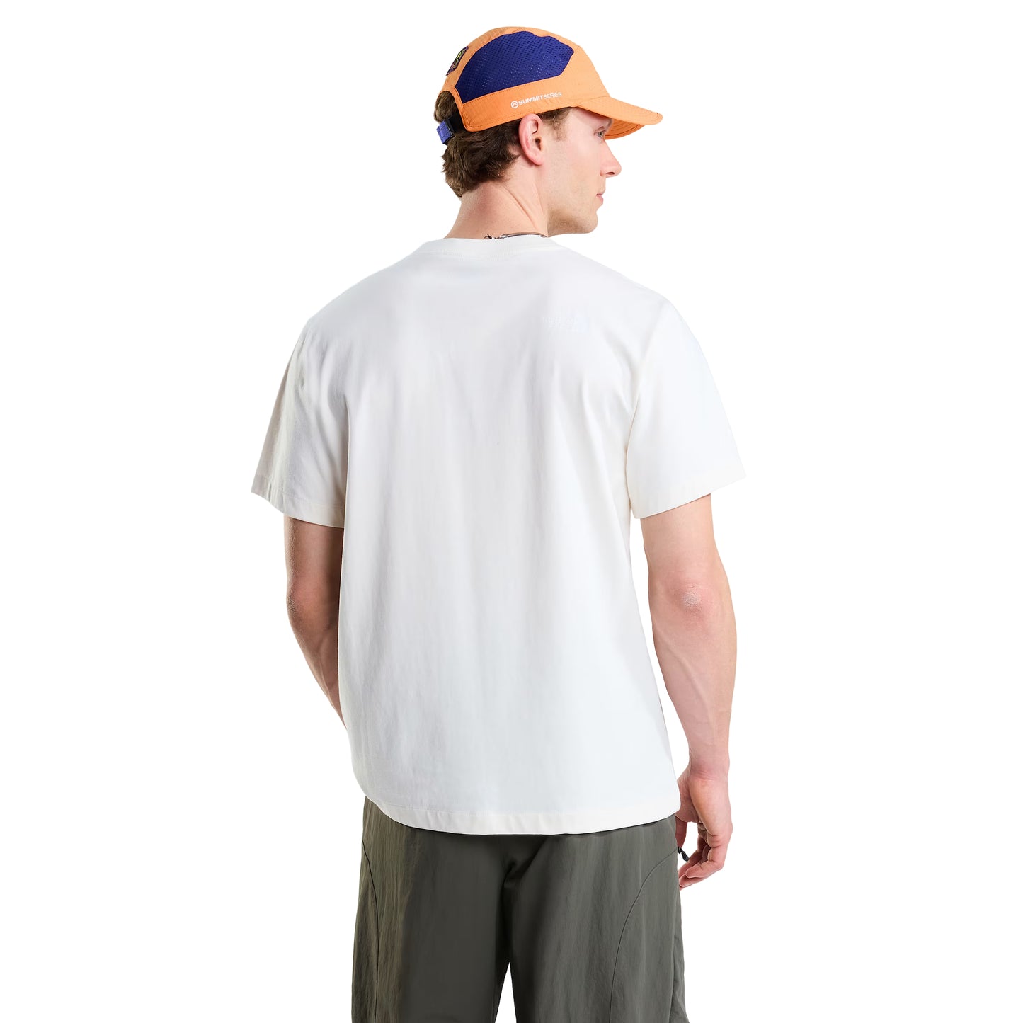 T-shirt unissexo The North Face Explorer Badges Relaxed em White Dune — modelo masculino de costas, boné técnico laranja e azul TNF, calções cargo verde-oliva, costas lisas em jersey White Dune, logótipo TNF estampado em serigrafia à base de água no ombro direito nas costas, corte relaxado com ombros descaídos visíveis, fundo branco.