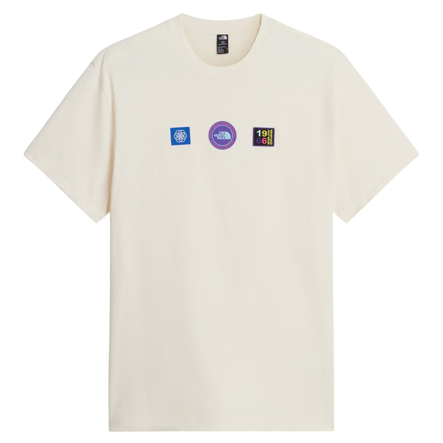 T-shirt unissexo The North Face Explorer Badges Relaxed em White Dune — vista frontal, produto sem modelo, três emblemas Explorer estampados em serigrafia à base de água no peito: emblema azul quadrado com globo à esquerda, emblema circular roxo "The North Face" ao centro, emblema retangular escuro "1966 Never Stop Exploring" com letras multicolor à direita, etiqueta TNF na gola interior visível, jersey White Dune 220 g/m² e gola canelada visíveis, fundo branco.