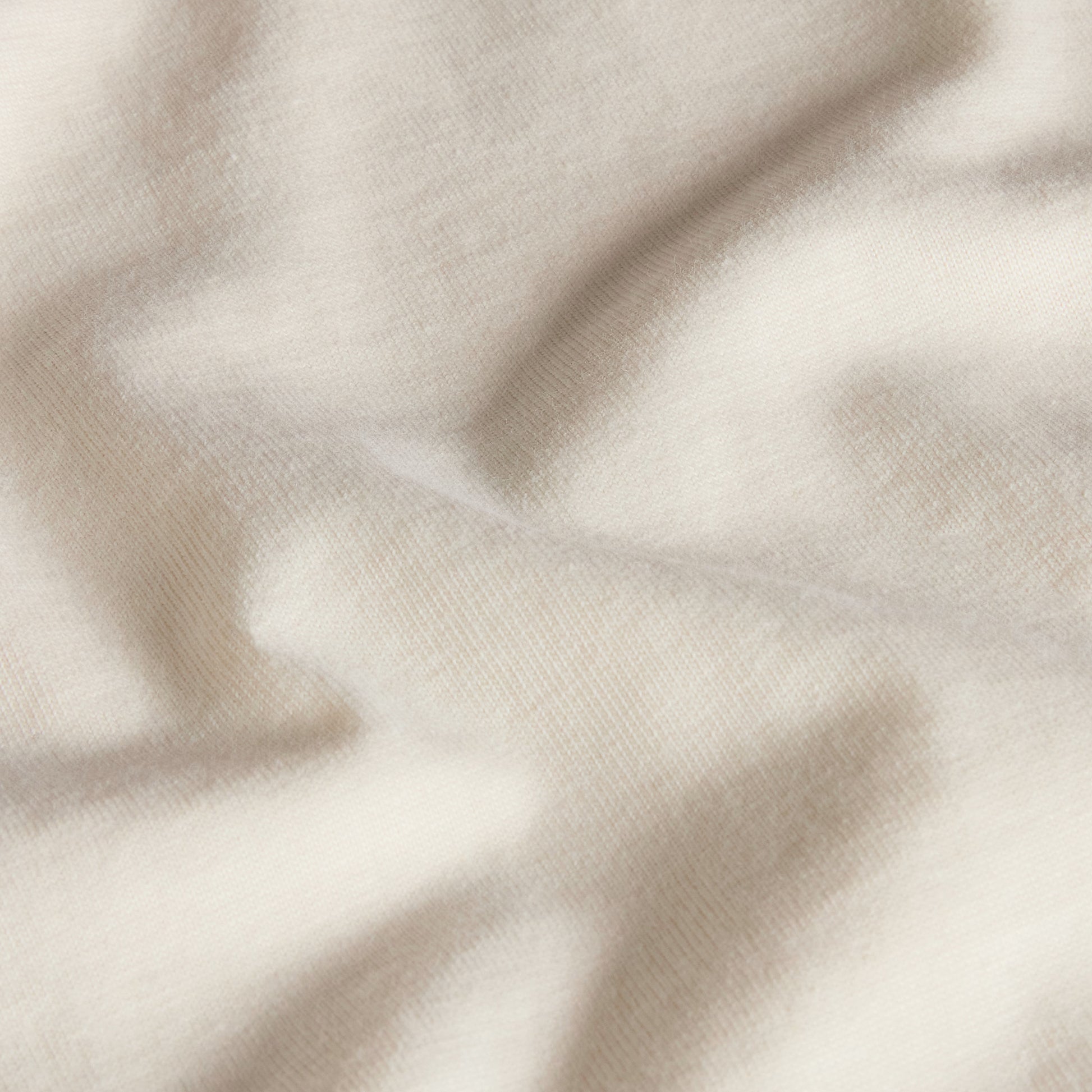 T-shirt unissexo The North Face Explorer Badges Relaxed em White Dune — detalhe da textura do jersey, close-up do tecido 100% algodão White Dune 220 g/m² com sombra de folhagem projetada, textura macia e estrutura do jersey visíveis, fundo neutro.