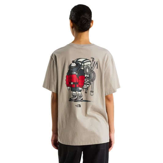 T-shirt The North Face Gear Up Get Out Relaxed em stone slab — modelo feminino de costas, corpo inteiro, gráfico de alpinista cartoon sobrecarregado de equipamento TNF impresso a serigrafia nas costas, logótipo The North Face abaixo do gráfico, calças escuras, fundo branco.