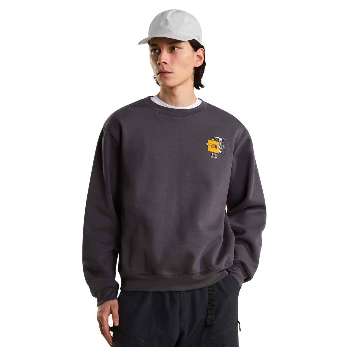 Sweatshirt unissexo The North Face Gear Up Get Out Relaxed Crew em Anthracite Grey — modelo masculino de frente, meio corpo superior, polar cinzento antracite, gráfico Gear Up Get Out em serigrafia à base de água com personagem de equipamento TNF em amarelo no peito esquerdo, boné cinzento claro, gola redonda canelada, corte relaxed, fundo branco.