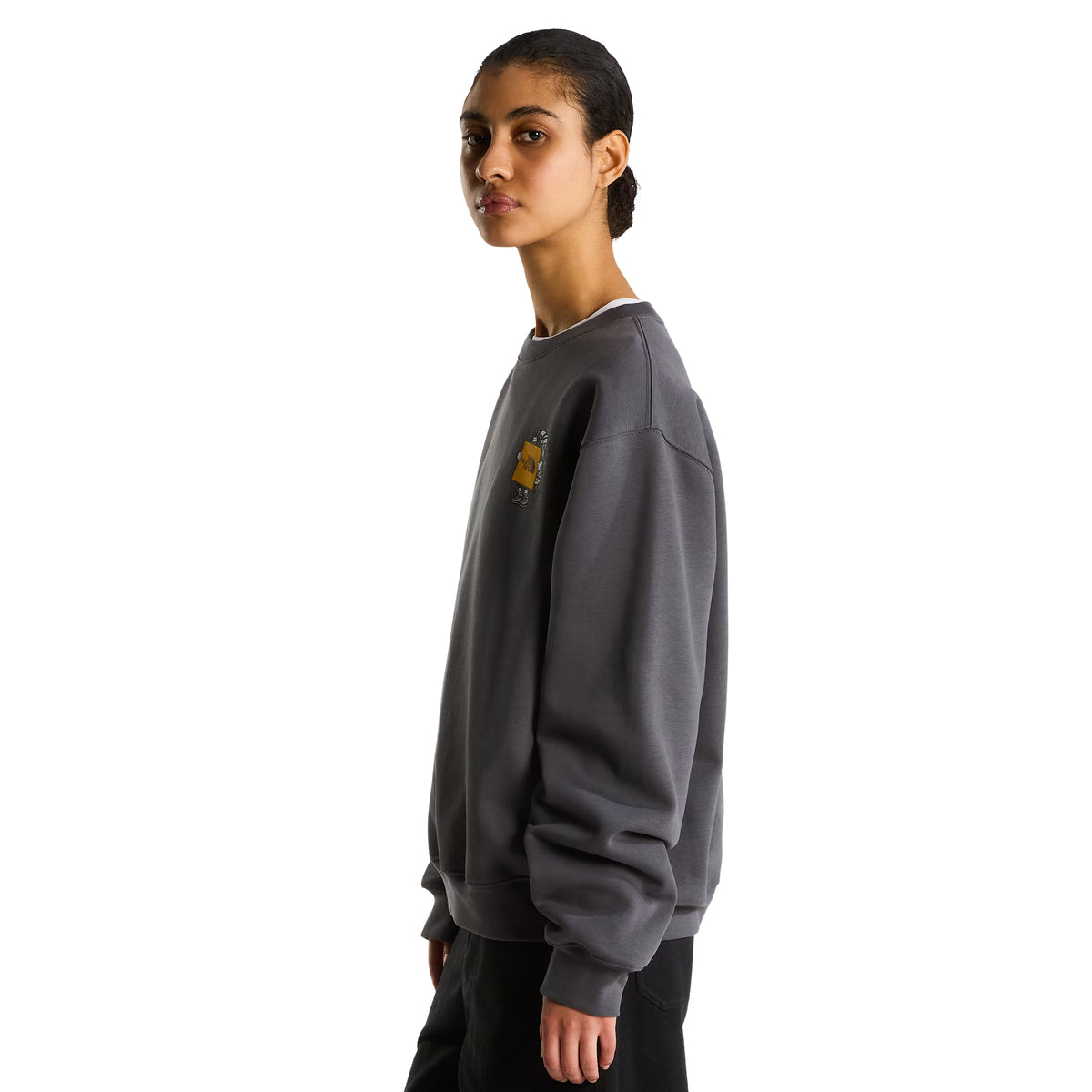 Sweatshirt unissexo The North Face Gear Up Get Out Relaxed Crew em Anthracite Grey — modelo feminino de perfil esquerdo, corpo inteiro, polar cinzento antracite, gráfico Gear Up Get Out em serigrafia à base de água parcialmente visível no peito, gola redonda canelada, corte relaxed com ombros descaídos, calças pretas, fundo branco.