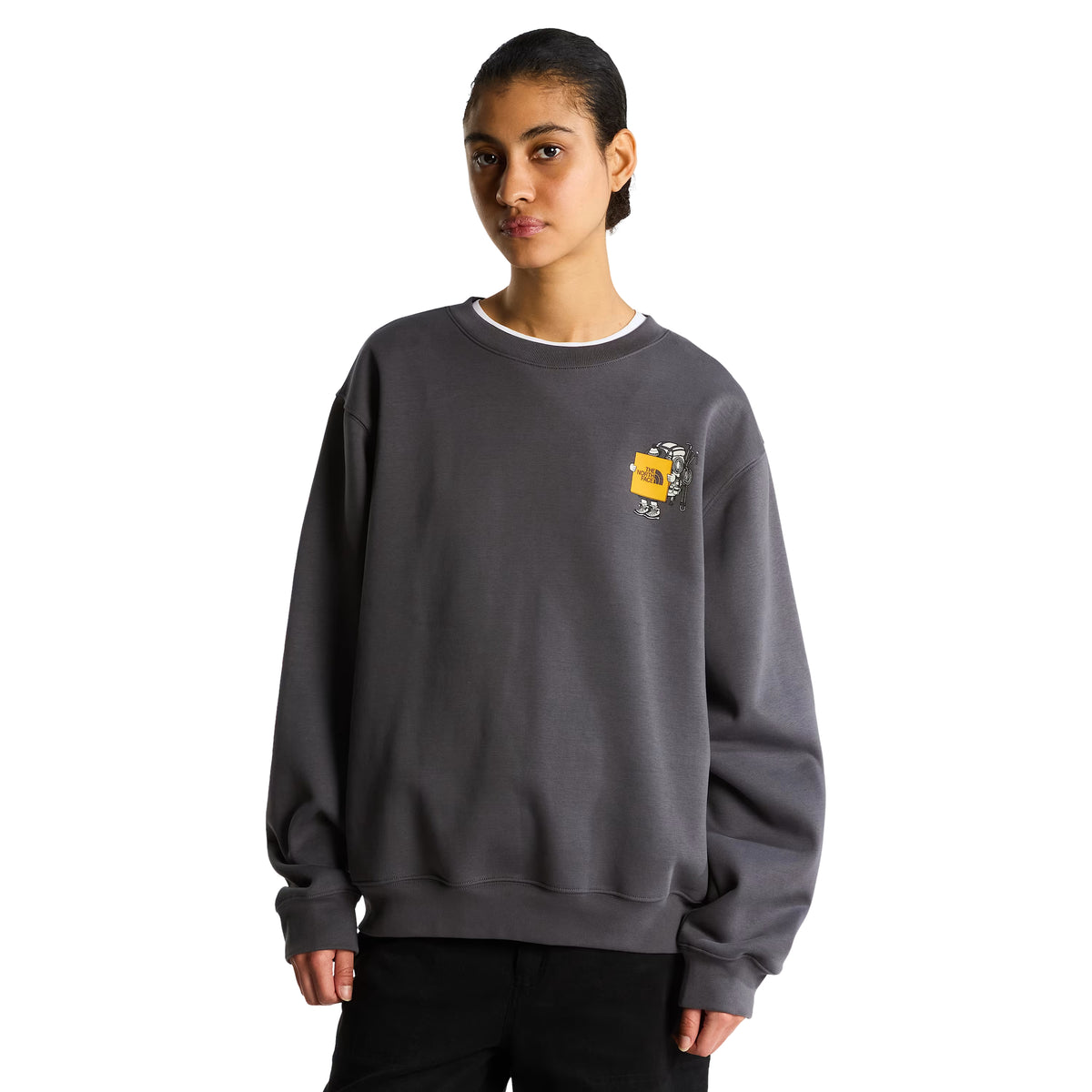 Sweatshirt unissexo The North Face Gear Up Get Out Relaxed Crew em Anthracite Grey — modelo feminino de frente, corpo inteiro, polar cinzento antracite, gráfico Gear Up Get Out em serigrafia à base de água com personagem de equipamento TNF em amarelo no peito esquerdo, gola redonda canelada, ombros descaídos, corte relaxed, calças pretas, fundo branco.