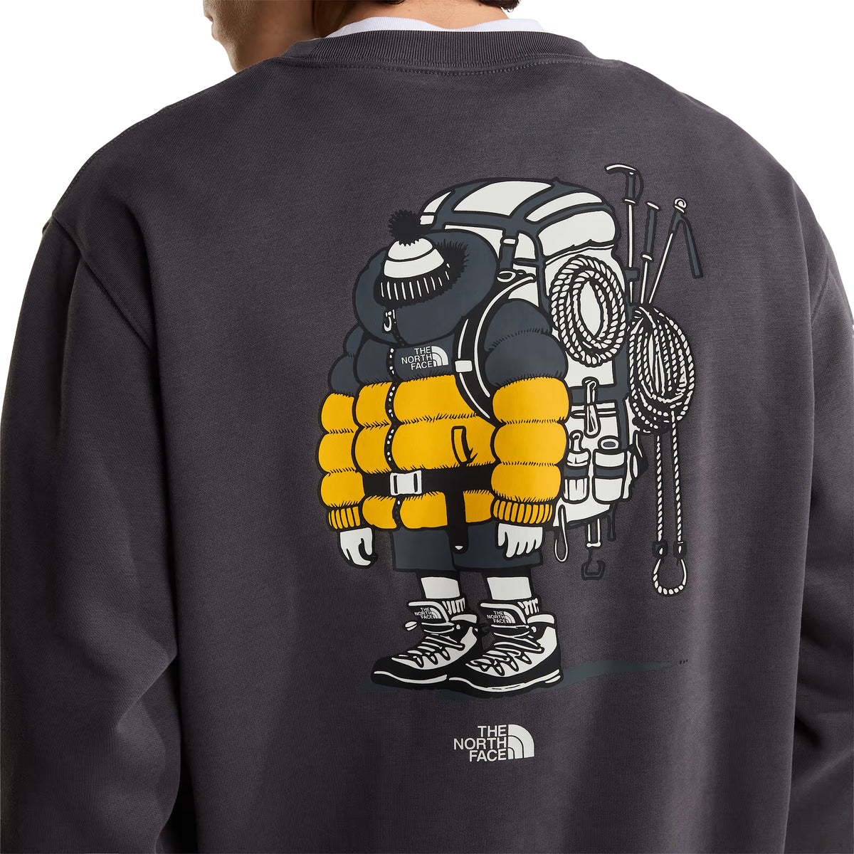 Sweatshirt unissexo The North Face Gear Up Get Out Relaxed Crew em Anthracite Grey — modelo masculino de costas, meio corpo superior, polar cinzento antracite, close-up do gráfico Gear Up Get Out em serigrafia à base de água nas costas com personagem de alpinista em amarelo e cinzento — casaco puffer amarelo, mochila, boné de malha, corda de escalada e picaretas —, logo The North Face em branco por baixo, gola canelada com t-shirt branca por baixo, fundo branco.
