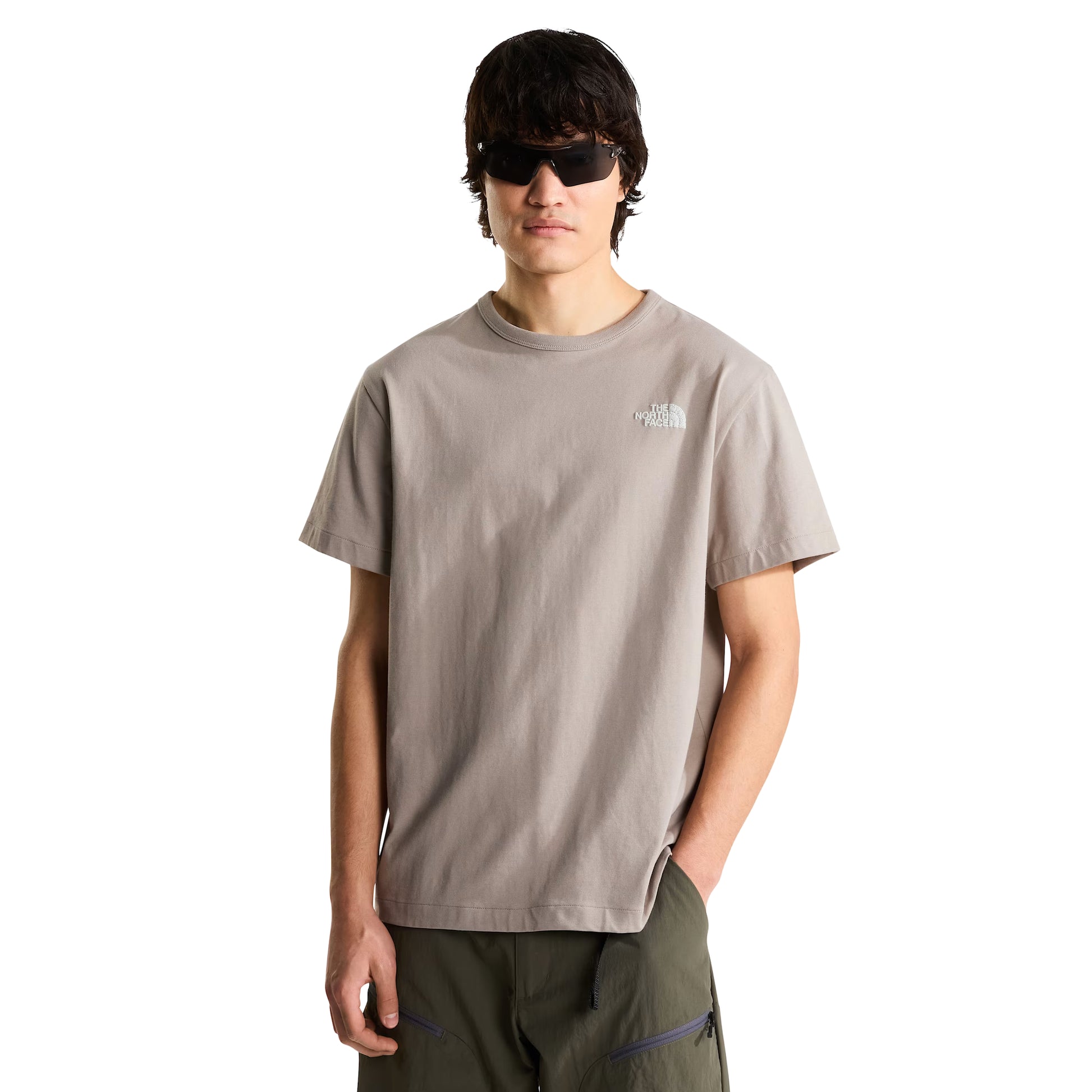 T-shirt The North Face NSE Slopes Relaxed em stone slab — modelo masculino de frente, corpo inteiro, corte relaxed, logótipo The North Face bordado a branco no peito esquerdo, gola redonda canelada, calças cargo verde military, óculos de sol escuros rectangulares, fundo branco.