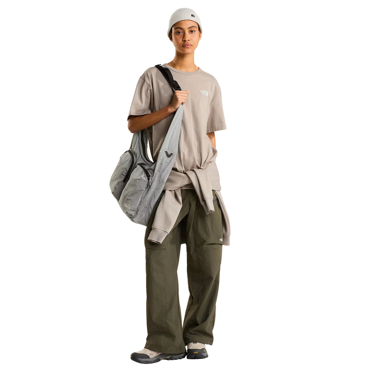 T-shirt The North Face NSE Slopes Relaxed em stone slab — modelo feminino de frente, corpo inteiro, corte relaxed oversized, mala The North Face cinzenta às riscas a tiracolo, gorro canelado branco, calças cargo verde military, sapatilhas cinzentas, fundo branco.