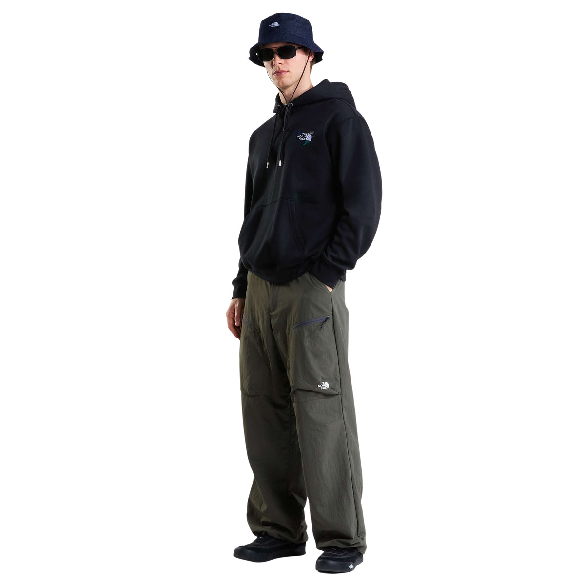 Modelo de corpo inteiro com sweat The North Face Off Piste Embro preta, calças cargo verde-escuras, chapéu e óculos de sol.