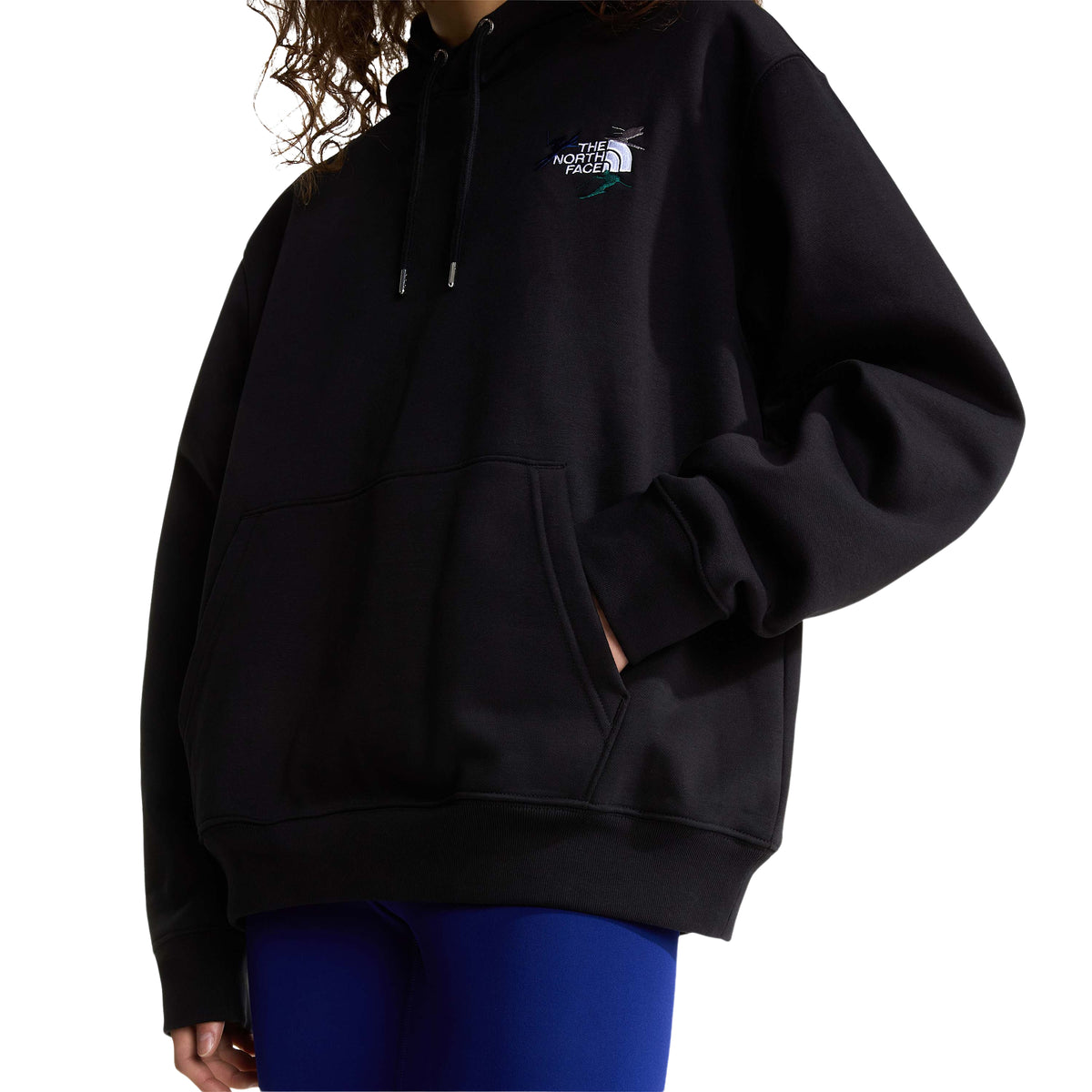 Pormenor da frente da sweat The North Face Off Piste Embro preta numa modelo, com bordado no peito e mão no bolso canguru.