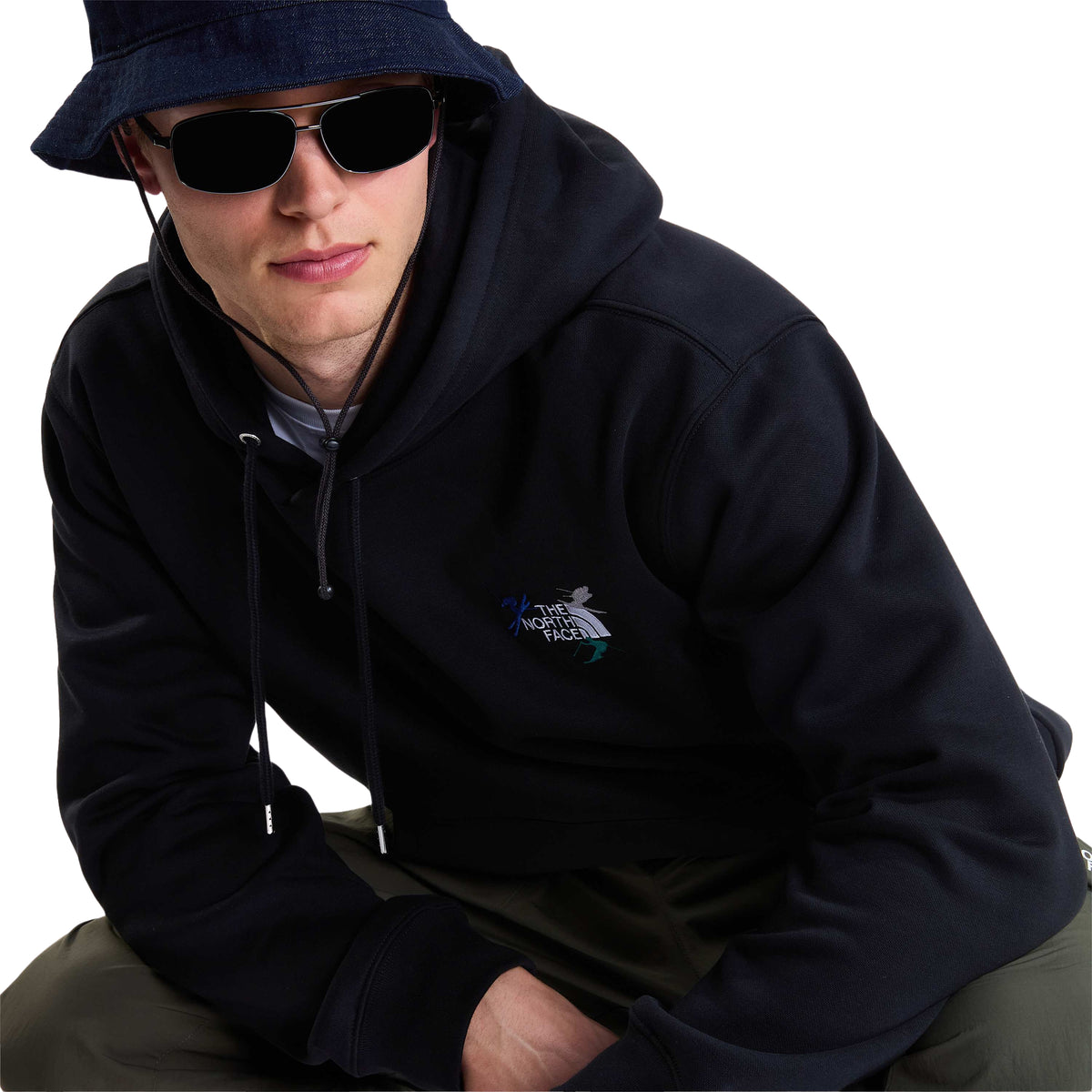 Modelo sentado com sweat The North Face Off Piste Embro preta, mostrando o bordado no peito e os cordões do capuz.